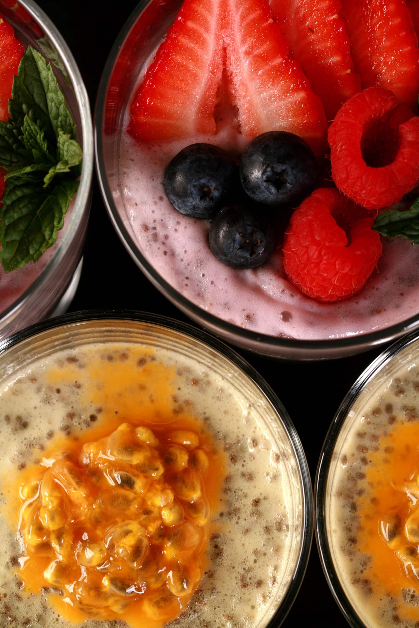 4 glasses of protein pudding with chia seeds. 2 are yellow and topped with passionfruit, the other two are pink and topped with berries.