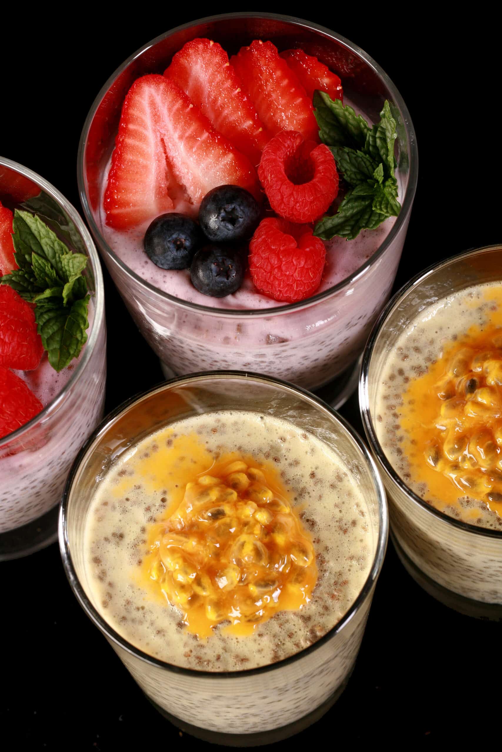 4 glasses of protein pudding with chia seeds. 2 are yellow and topped with passionfruit, the other two are pink and topped with berries.