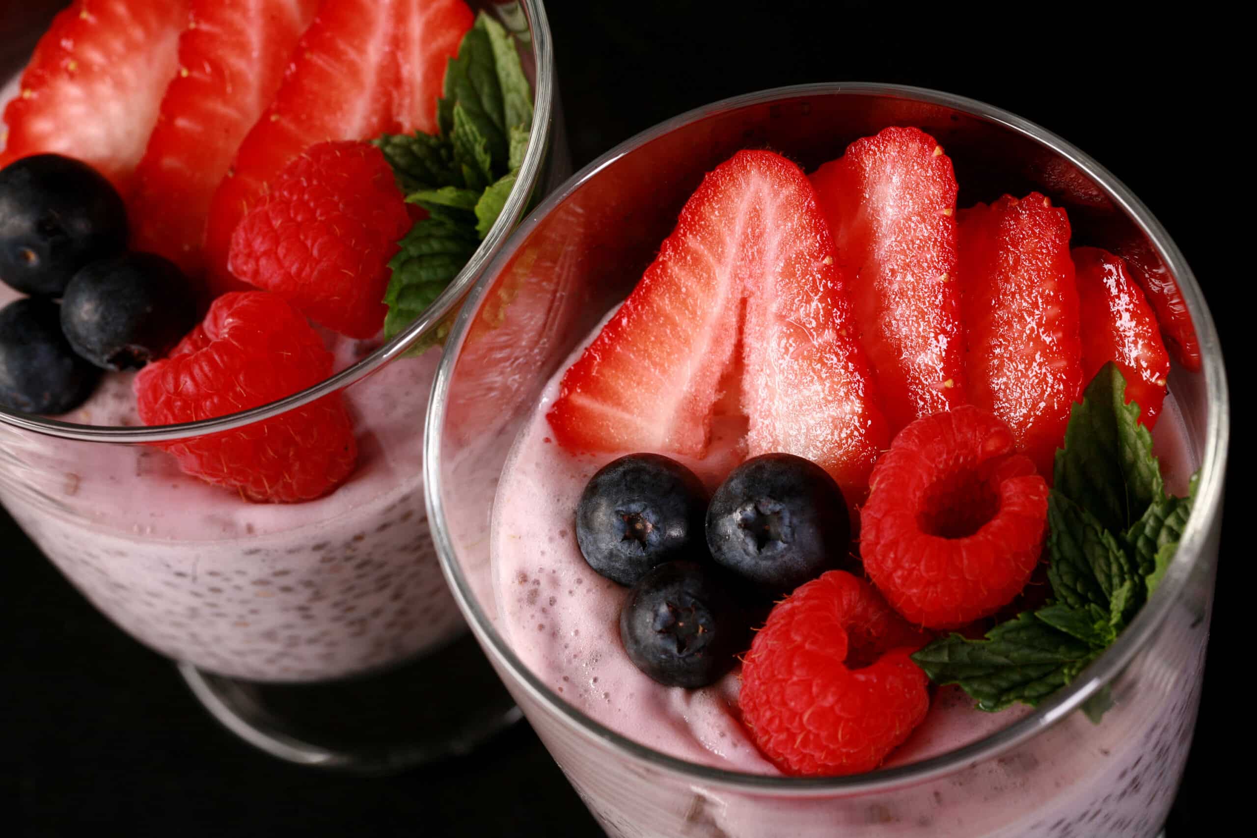 2 glasses of berry protein pudding, topped with strawberry slices, raspberries, and blueberries.