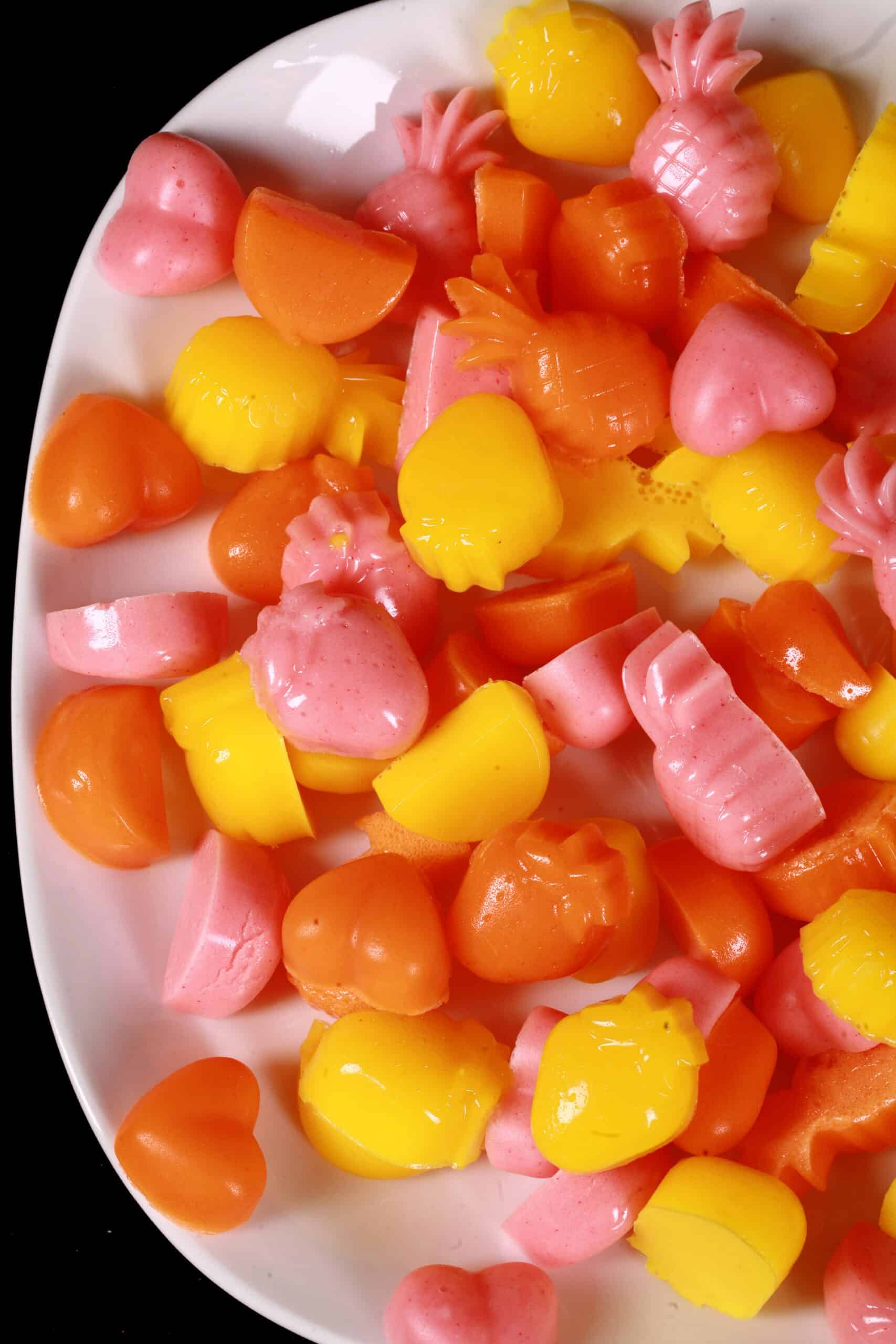 A plate of pink, orange, and yellow protein gummy candies in a variety of fruit and heart shapes.