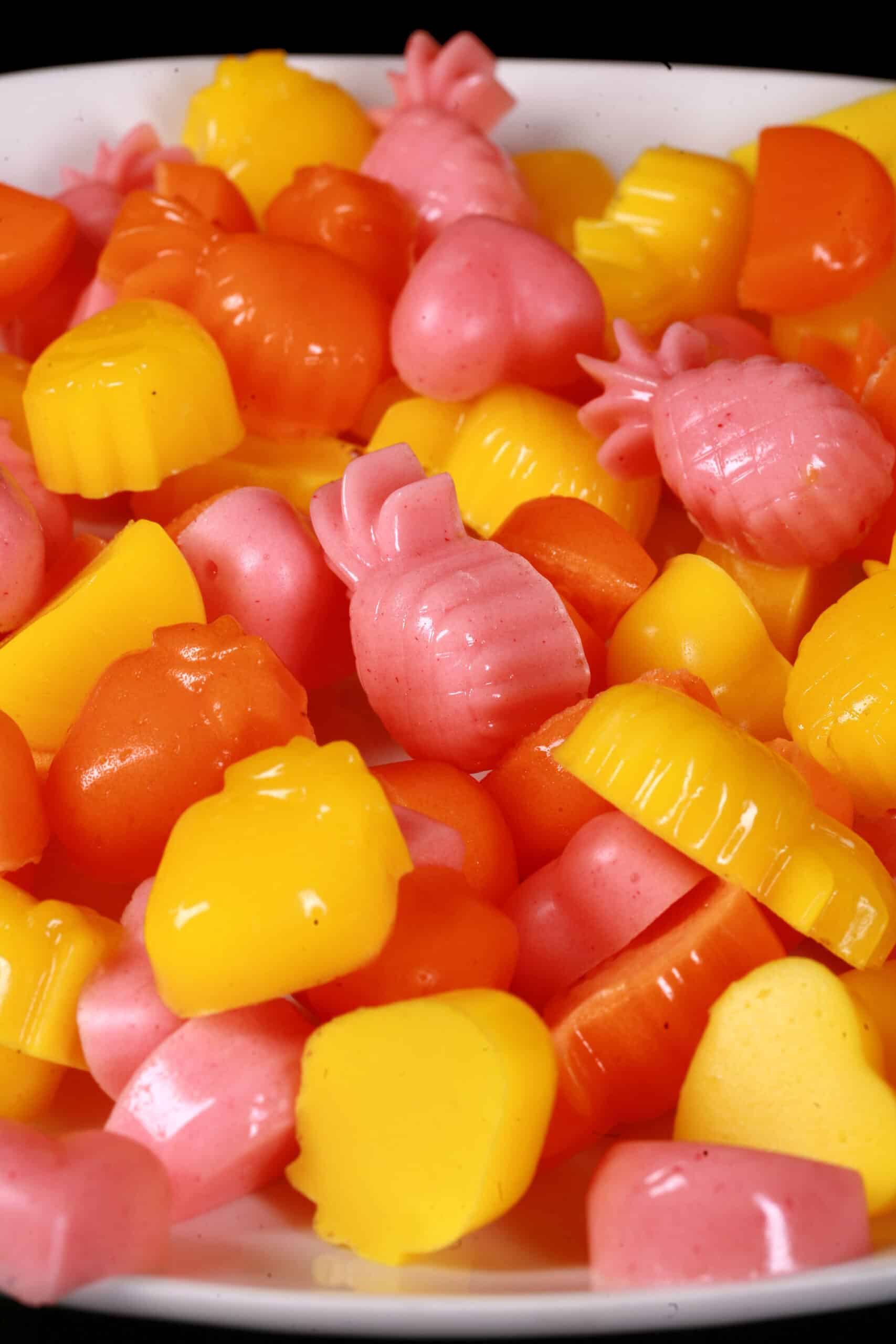 A plate of pink, orange, and yellow protein gummies in a variety of fruit and heart shapes.