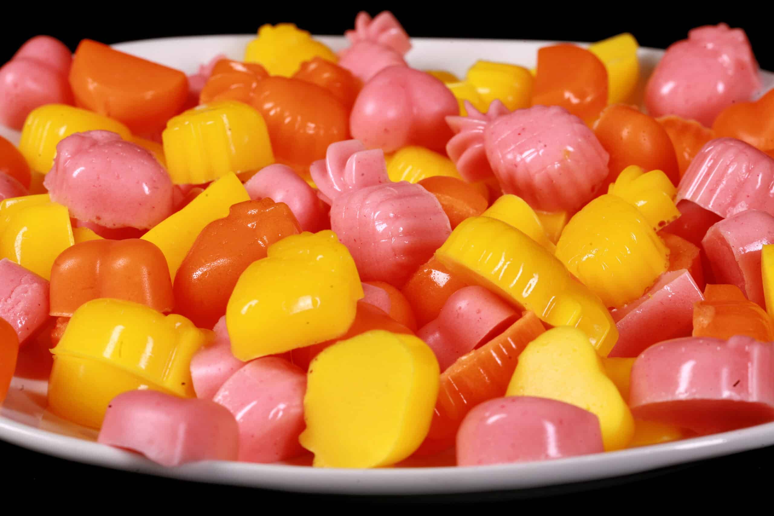 A plate of pink, orange, and yellow protein gummies in a variety of fruit and heart shapes.