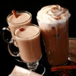 2 mugs of protein chai latte and a tall glass of protein chai latte, along with several packets of keto chai latte mix.