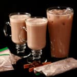 2 mugs of protein powder pumpkin chai latte, a tall glass of protein iced pumpkin chai latte, and several bags of mix.