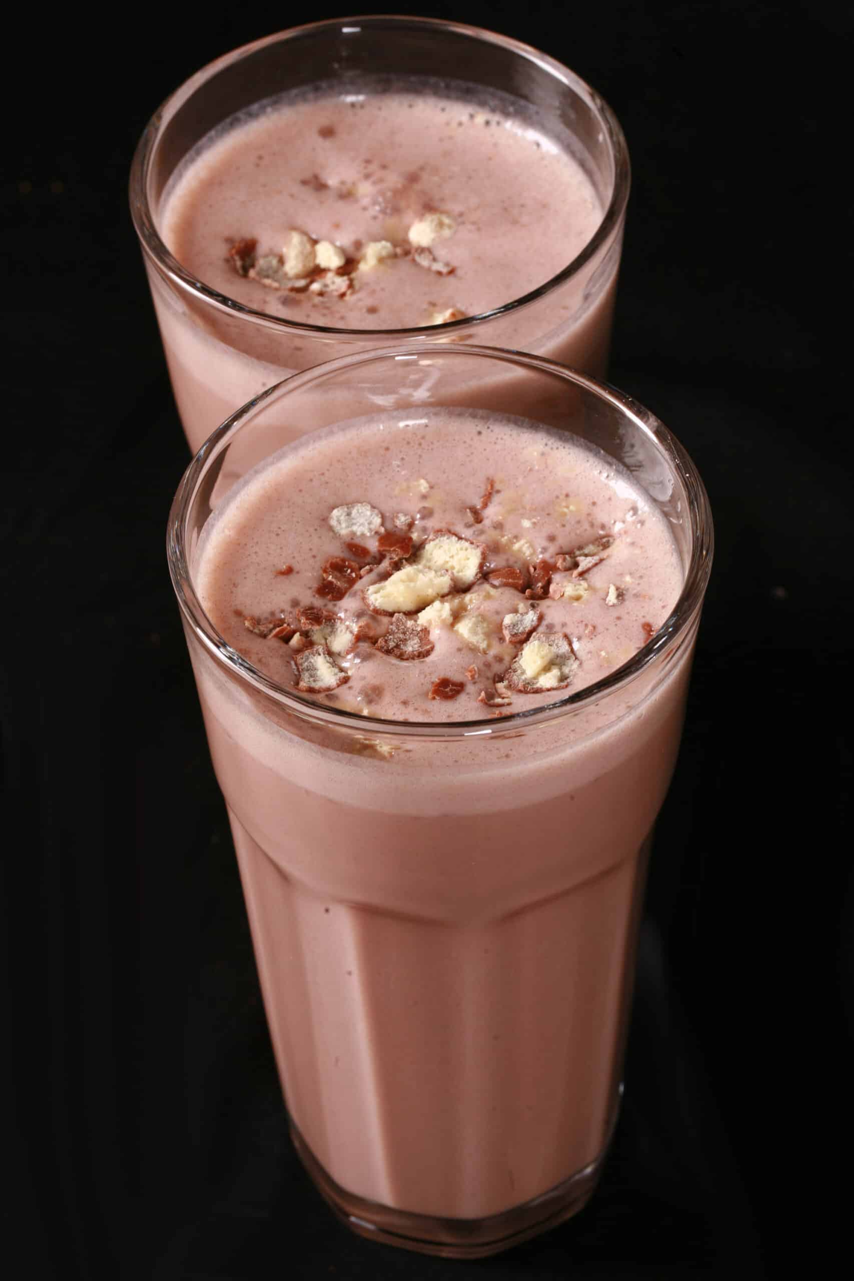 2 tall glasses of chocolate malt protein shakes with crushed Whoppers Malted milk balls candy on top.