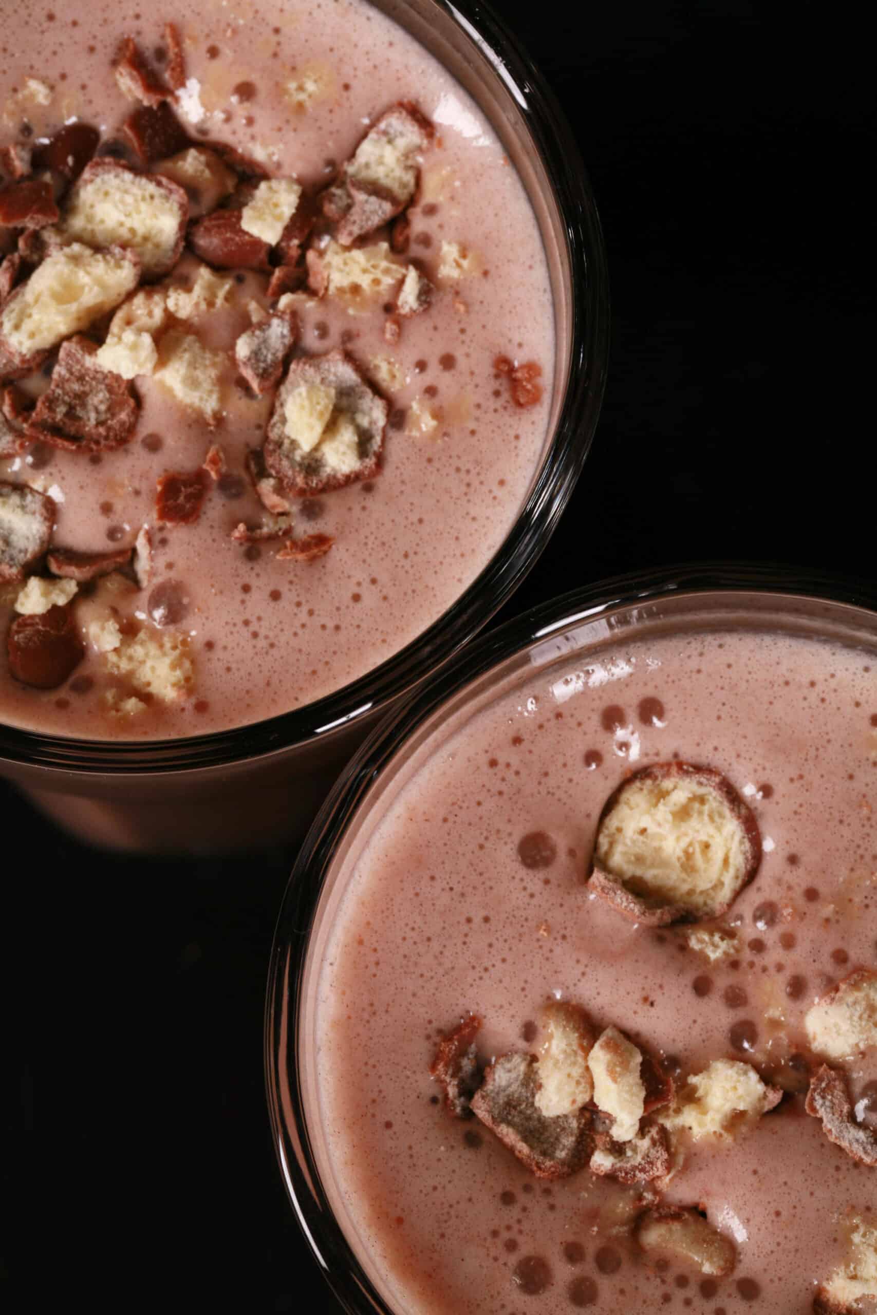 2 tall glasses of chocolate malt protein shakes with crushed Whoppers Malted milk balls candy on top.
