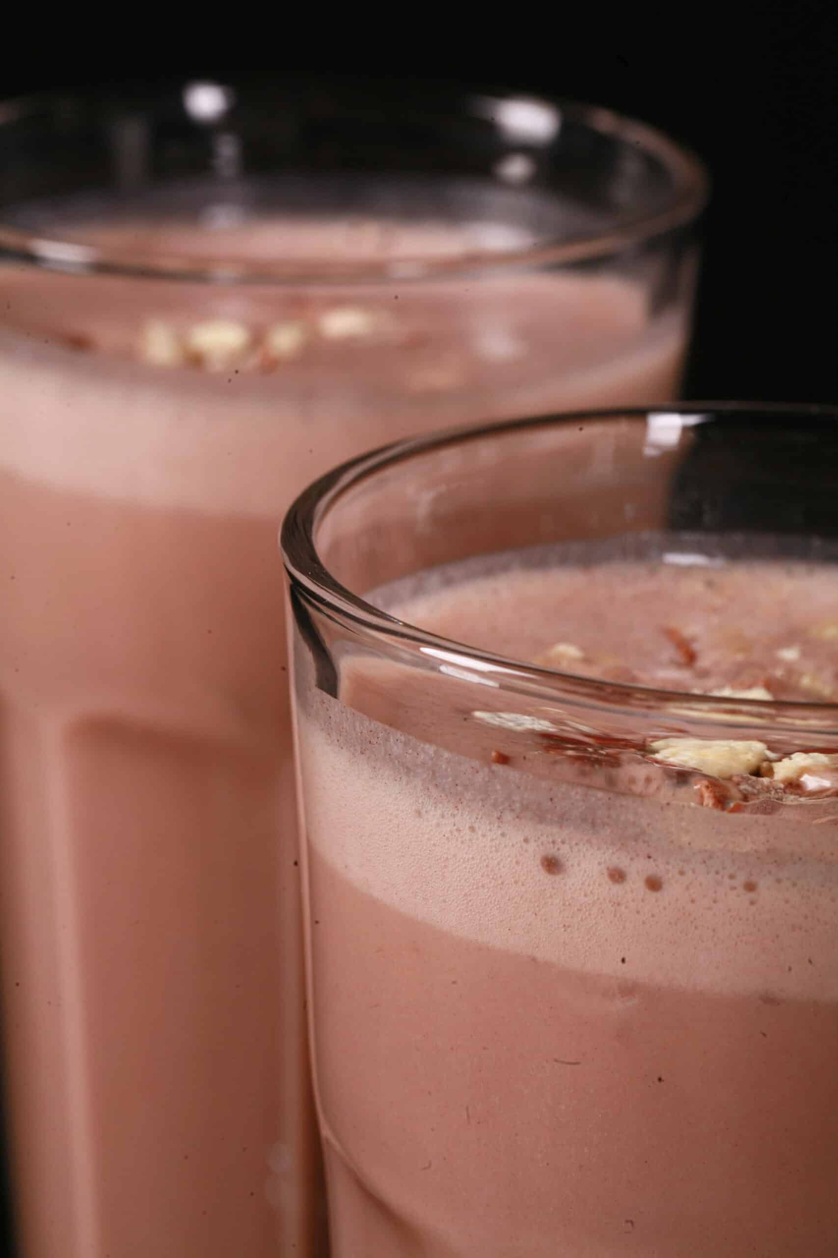 2 tall glasses of chocolate malt protein shakes with crushed Whoppers Malted milk balls candy on top.