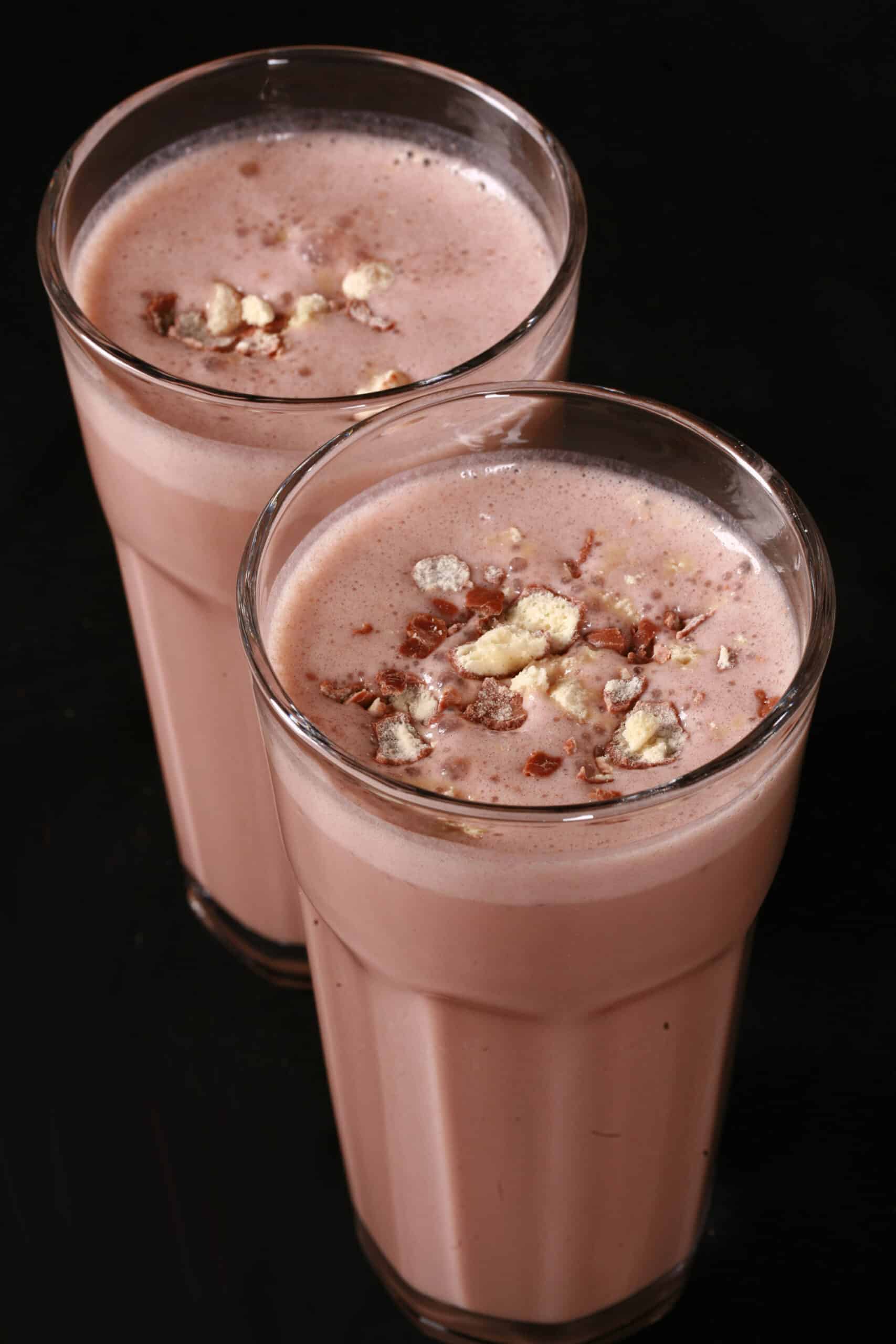 2 tall glasses of chocolate malt protein shakes with crushed Whoppers Malted milk balls candy on top.