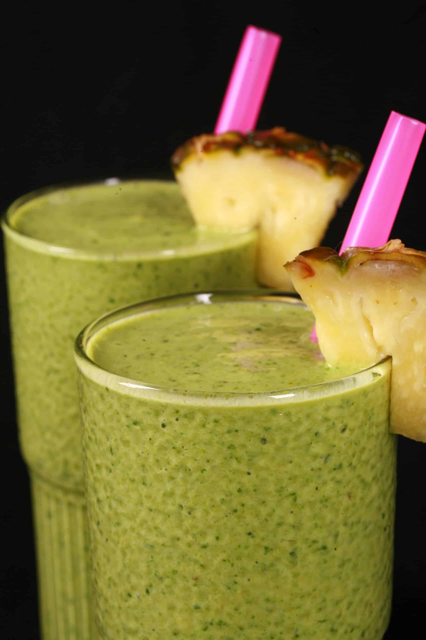 2 tall glasses of high protein tropical green smoothies, garnished with fresh pineapple wedges and pine straws.
