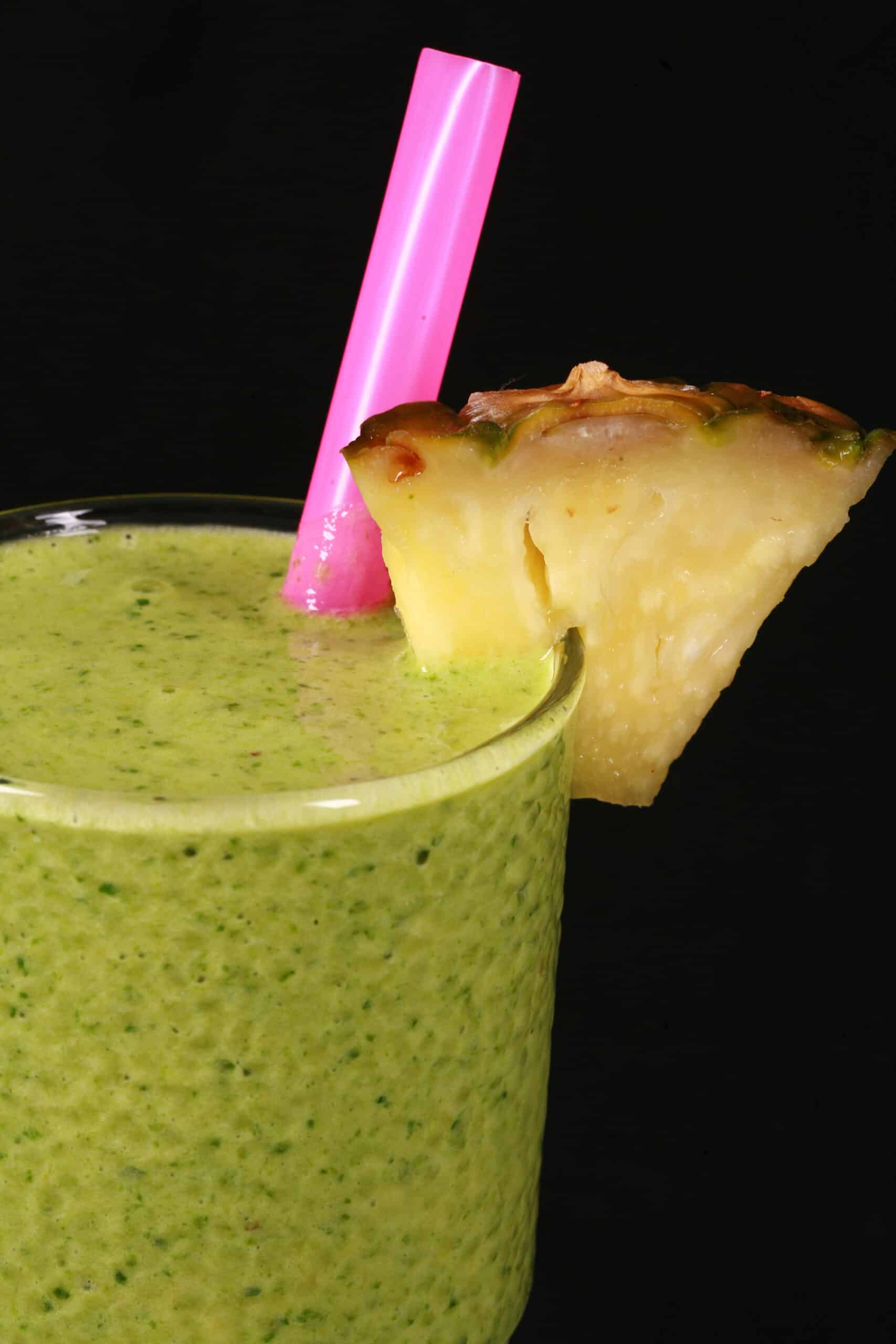 2 tall glasses of tropical green protein smoothies, garnished with fresh pineapple wedges and pink straws.