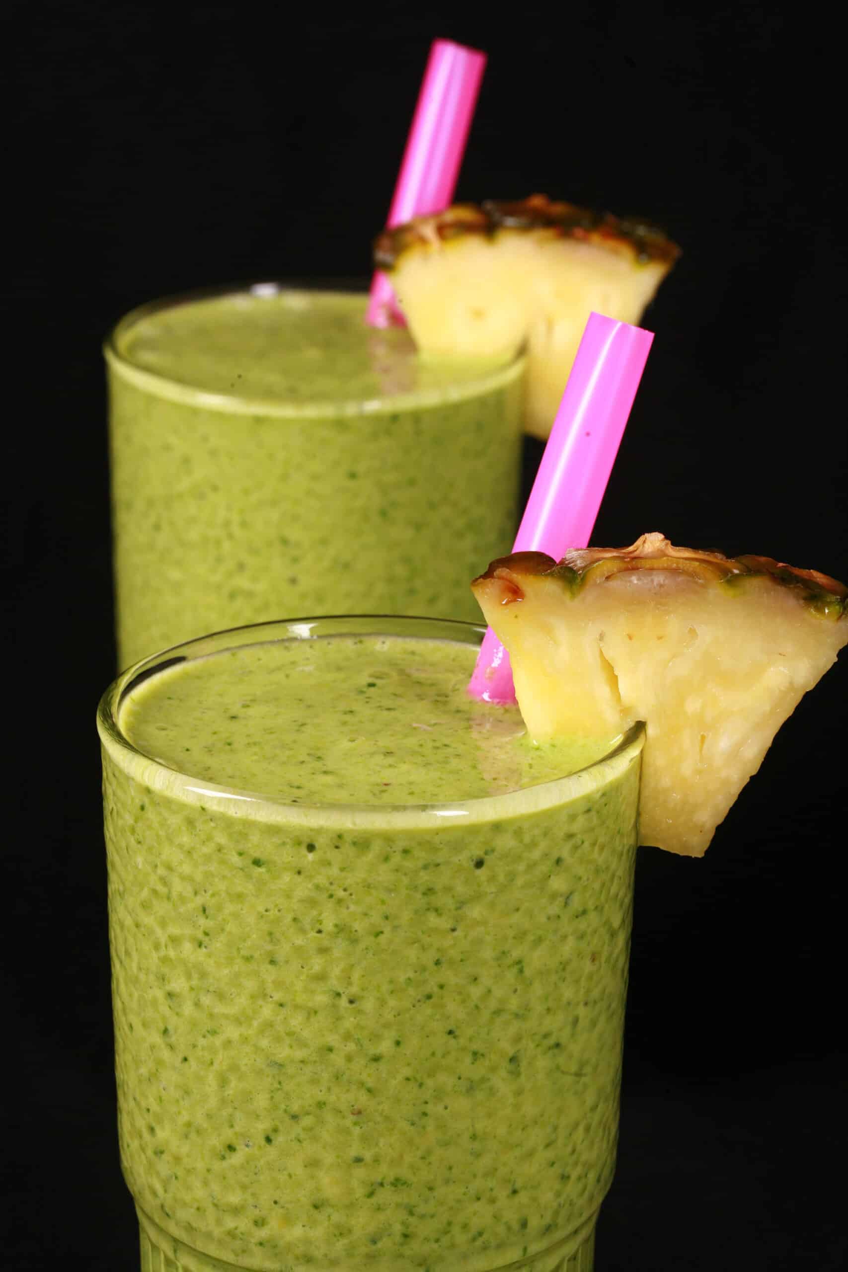 2 tall glasses of high protein tropical green smoothies, garnished with fresh pineapple wedges and pink straws.