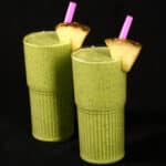2 tall glasses of high protein tropical green smoothies, garnished with fresh pineapple wedges and pink straws.