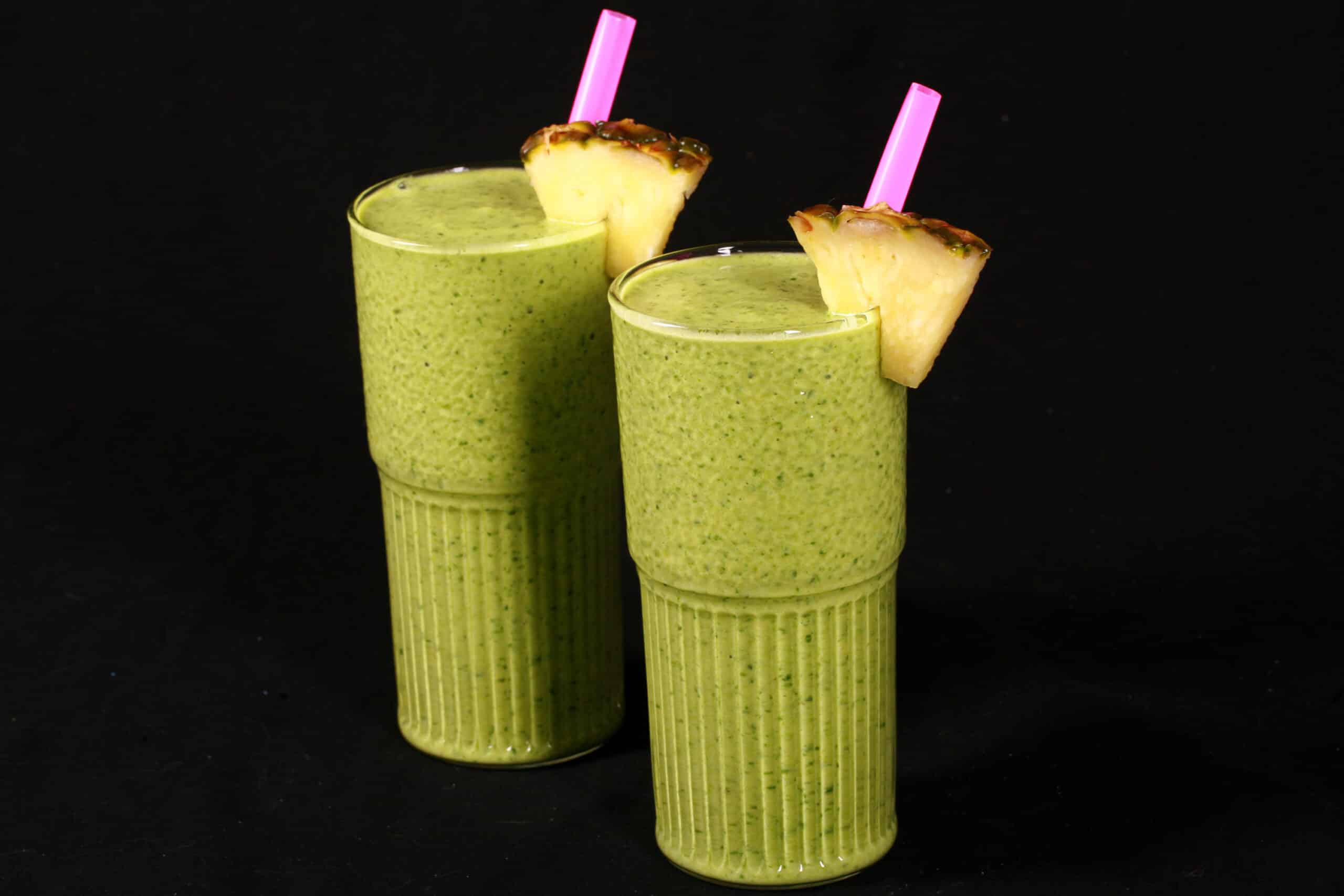 2 tall glasses of high protein tropical green smoothies, garnished with fresh pineapple wedges and pink straws.