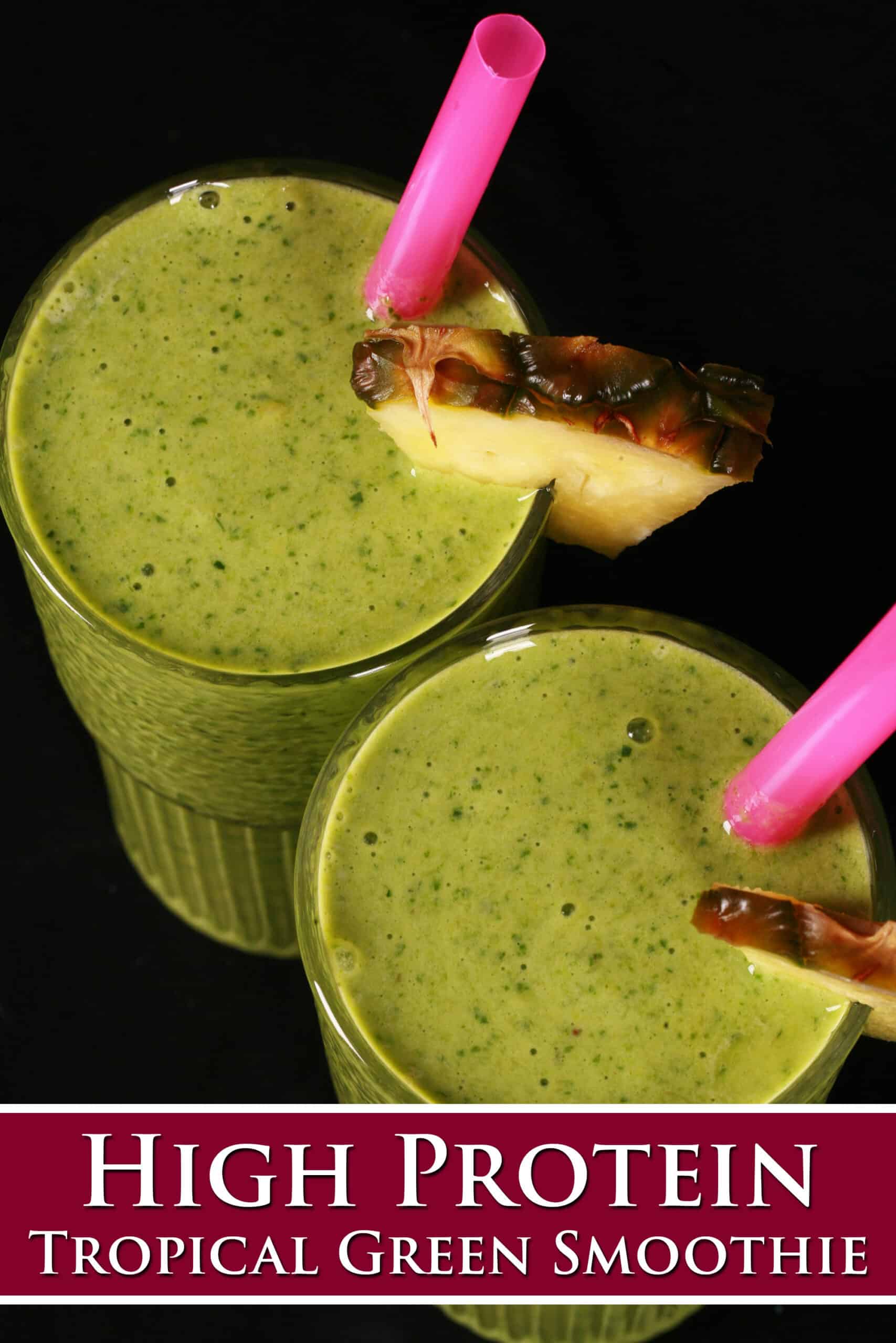 2 tall glasses of tropical green protein smoothies, garnished with fresh pineapple wedges and pink straws.  Overlaid text says high protein tropical green smoothie.