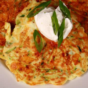 3 high protein zucchini pancakes on a plate, topped with sour cream and green onions.