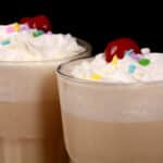 2 tall glasses of malted milk protein shakes garnished with whipped cream, sprinkles, and a maraschino cherry.