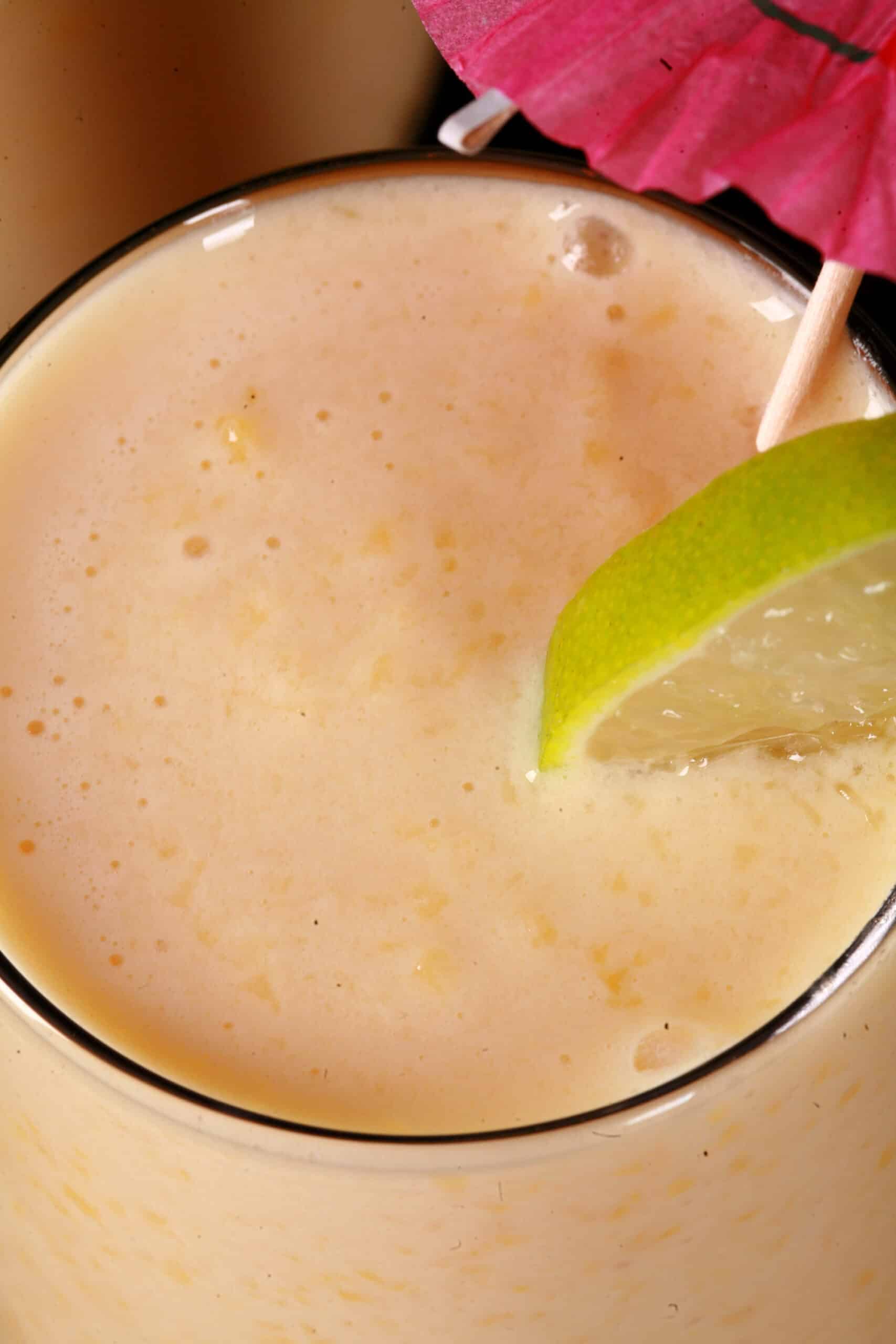 2 tall glasses of mango daiquiri protein smoothie, garnished with lime slices and pink cocktail umbrellas.