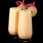 2 tall glasses of mango daiquiri protein smoothie, garnished with lime slices and pink cocktail umbrellas.