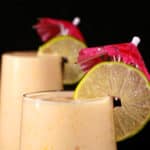 2 tall mango daiquiri protein smoothies, garnished with lime slices and pink cocktail umbrellas.