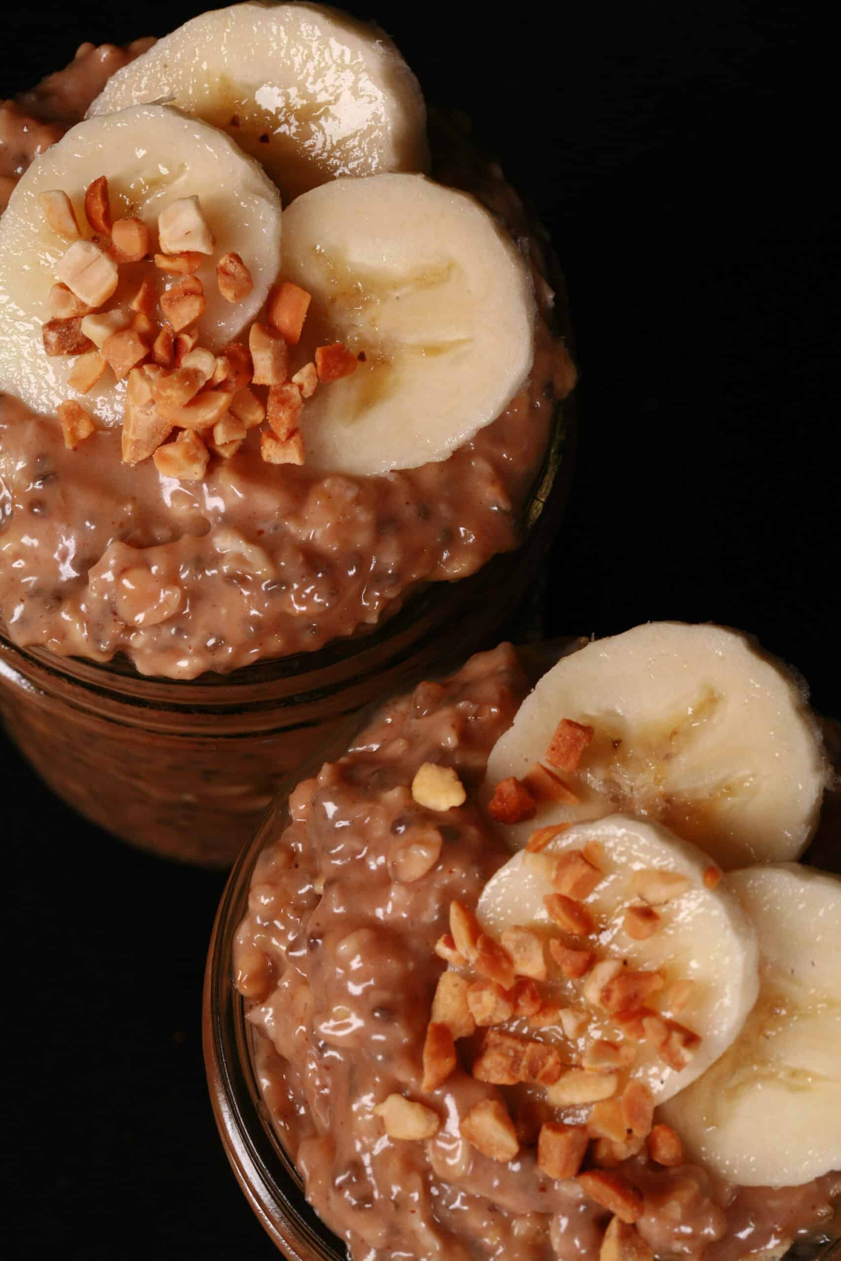 2 jars of high protein peanut butter and banana overnight oats, garnished with banana slices and chopped peanuts.