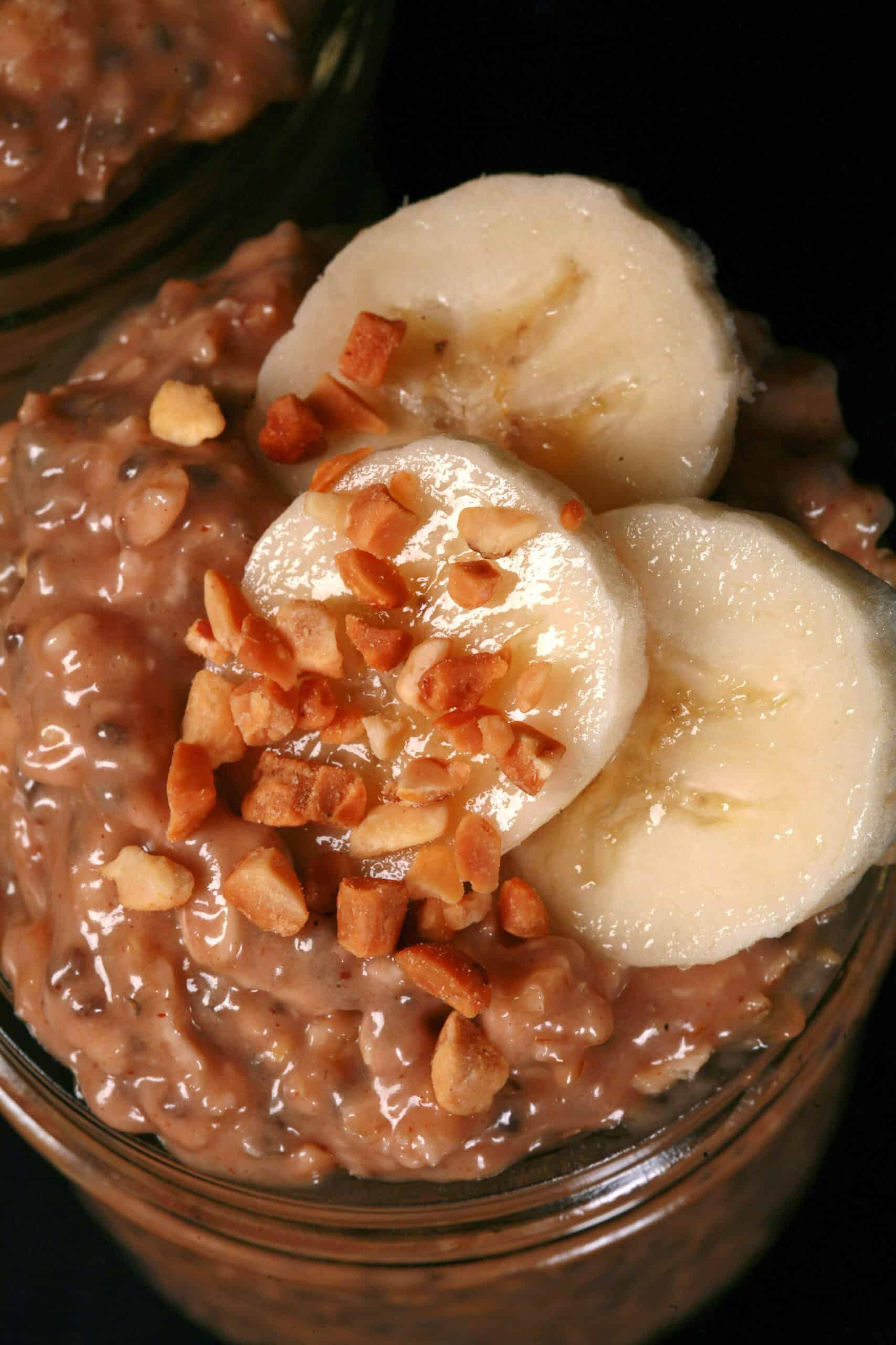 A jar of high protein peanut butter and banana overnight oatmeal, garnished with banana slices and chopped peanuts.