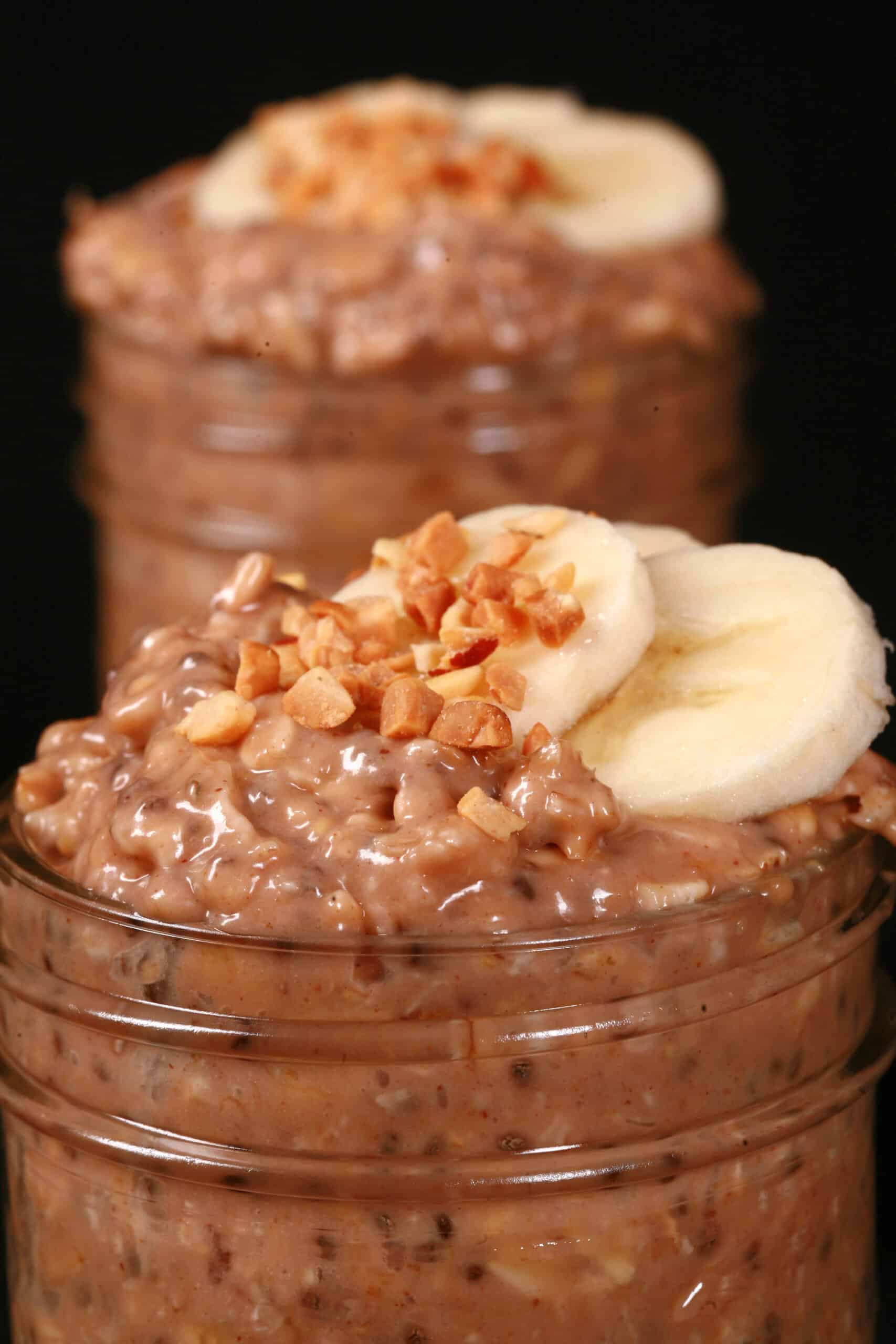 2 jars of high protein peanut butter and banana overnight oats, garnished with banana slices and chopped peanuts.