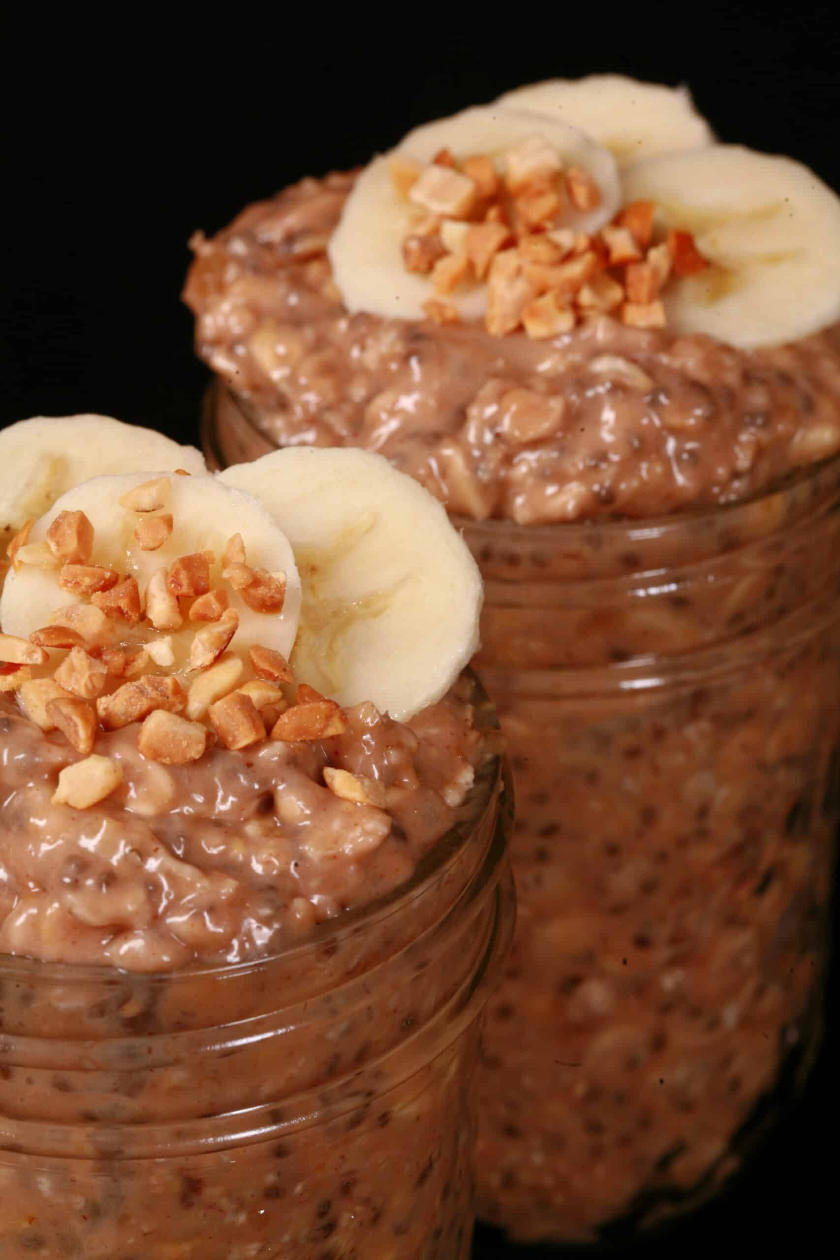 2 jars of high protein peanut butter and banana overnight oats, garnished with banana slices and chopped peanuts.