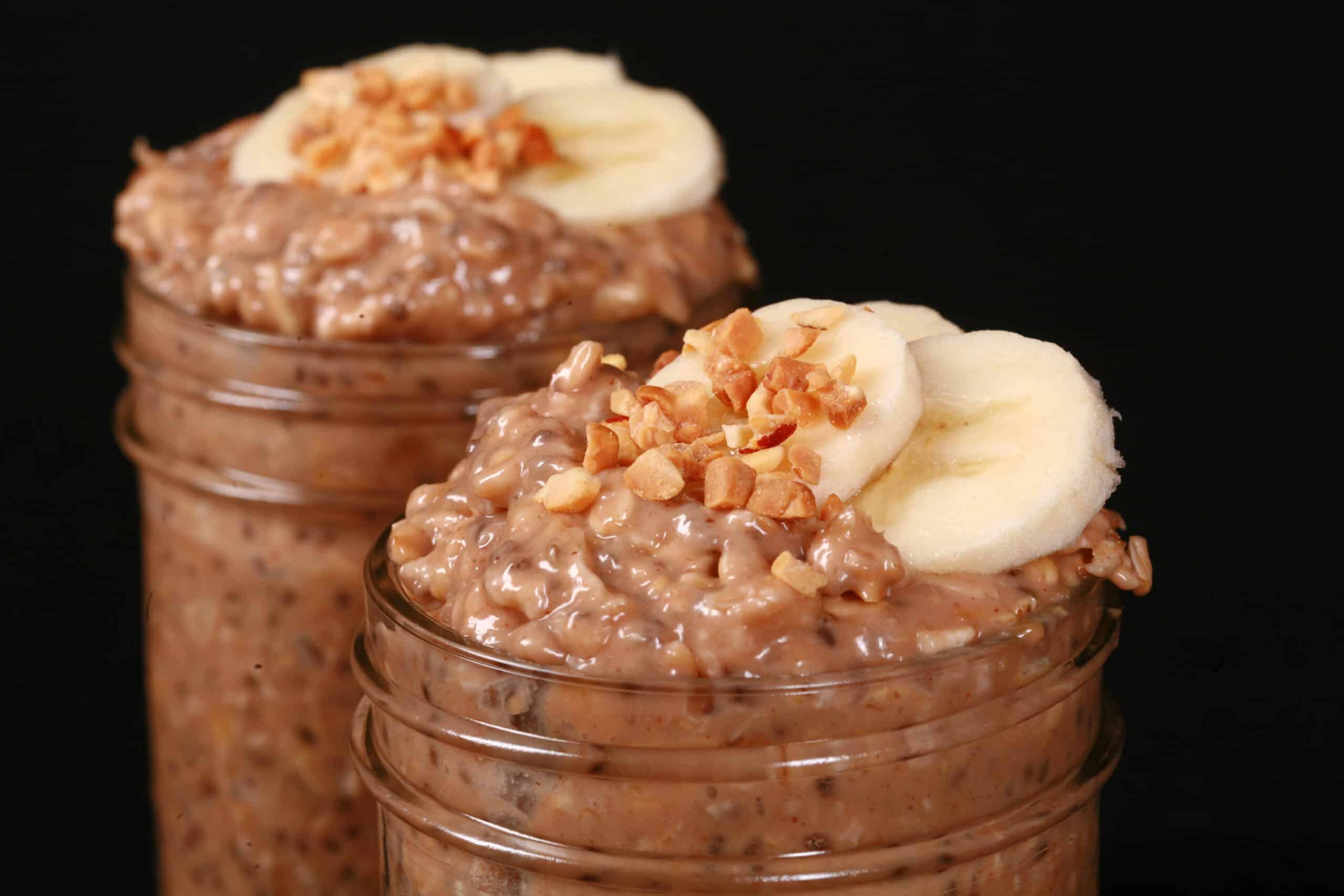 2 jars of high protein peanut butter and banana overnight oats, garnished with banana slices and chopped peanuts.