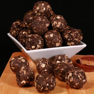A bowl of peanut butter cup protein balls, with more on the cutting board it's sitting on.