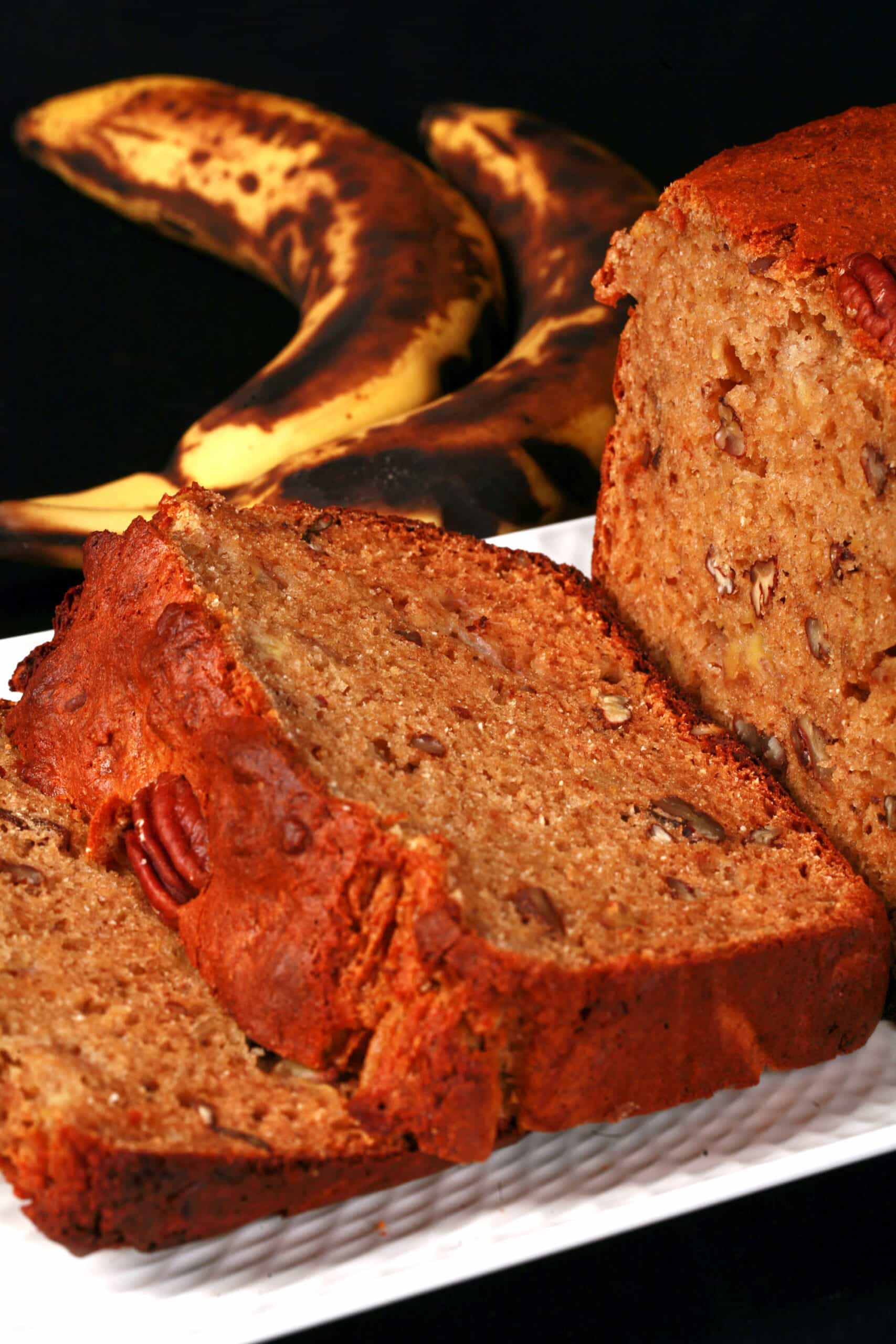 A sliced loaf of gluten free high protein banana nut bread on a white plate.