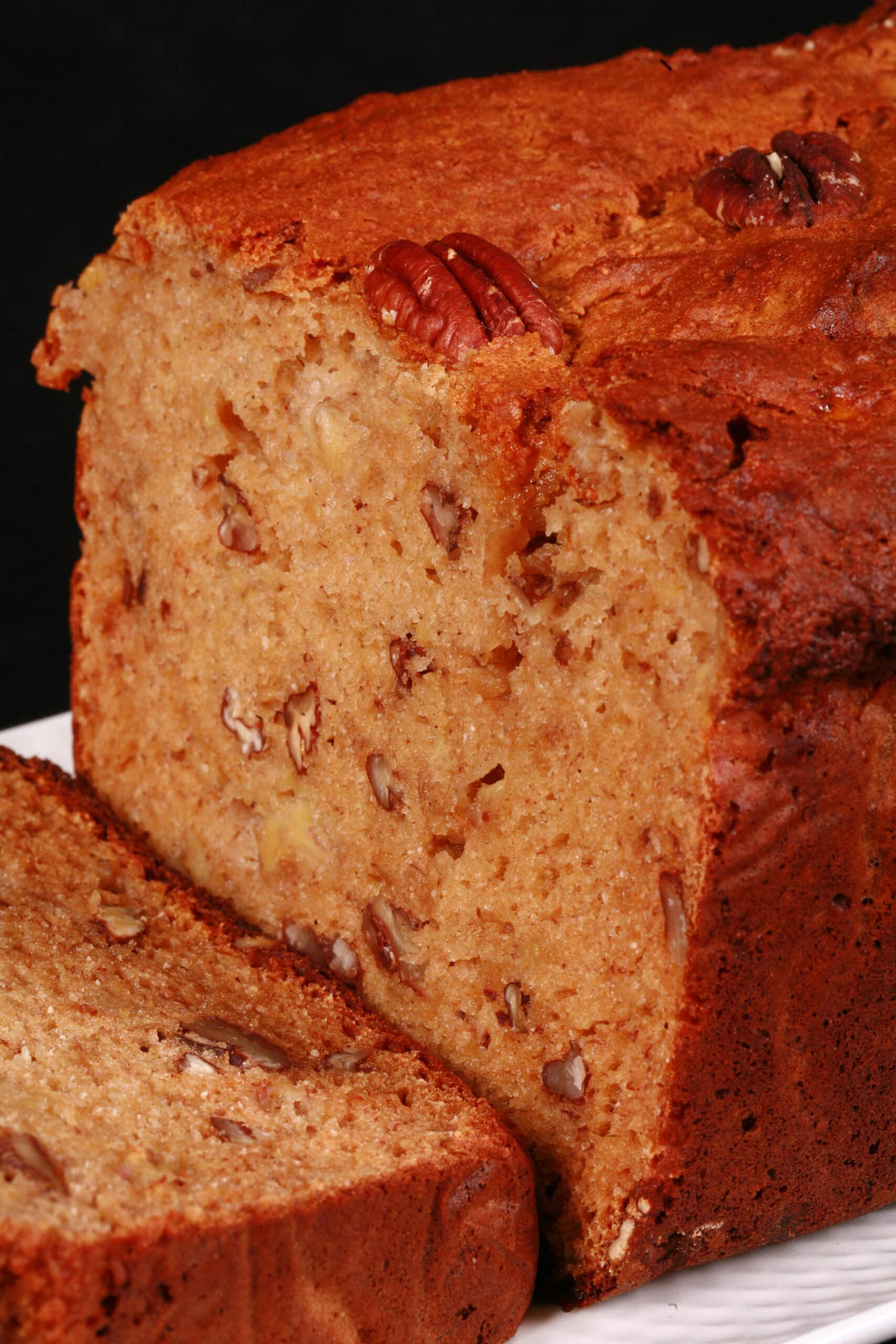 A sliced loaf of gluten free high protein banana nut bread on a white plate.