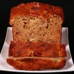 A sliced loaf of gluten free high protein banana nut bread on a white plate.