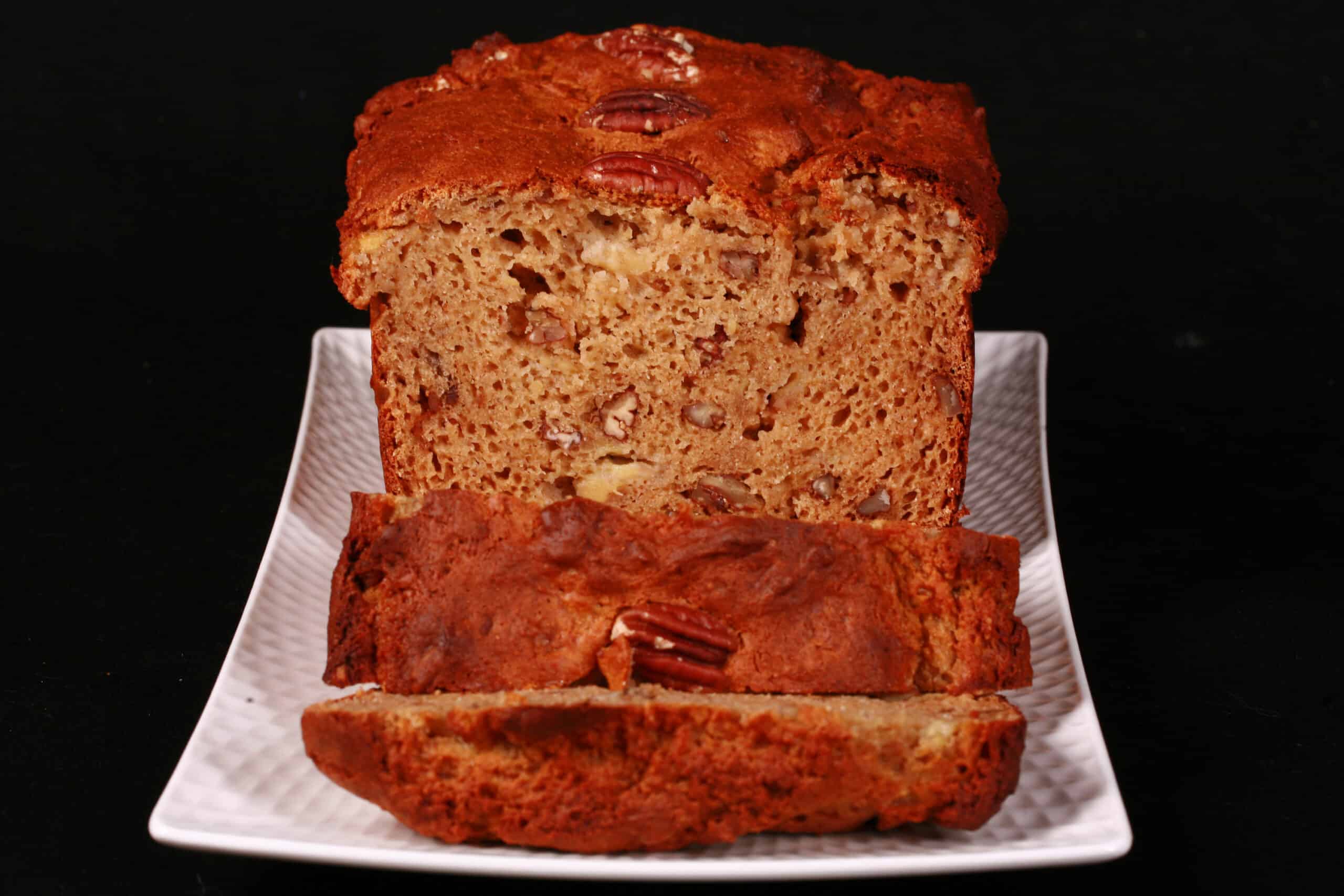 A sliced loaf of gluten free high protein banana nut bread on a white plate.