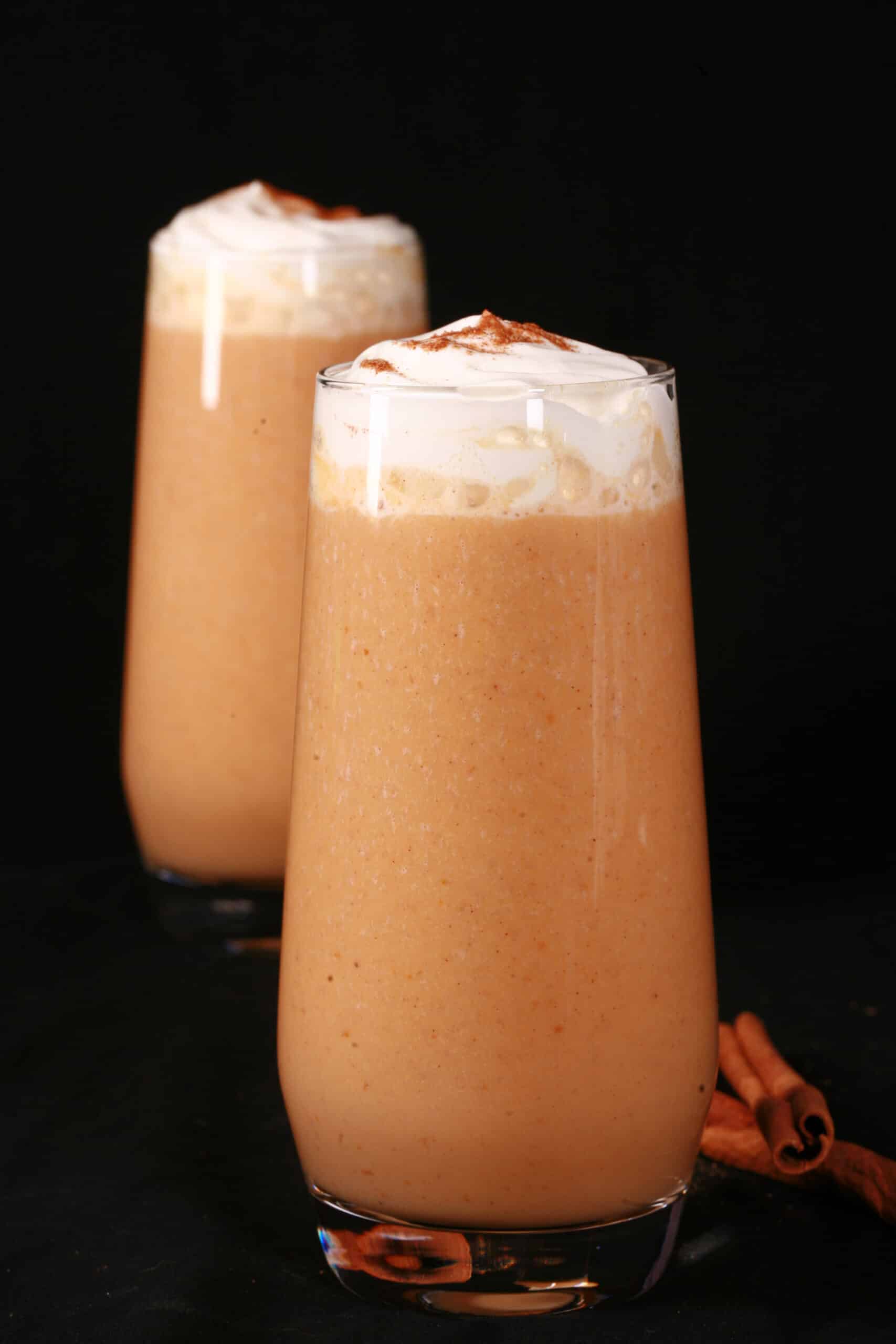 2 pumpkin pie protein shakes in tall glasses, topped with whipped cream and pumpkin spice.