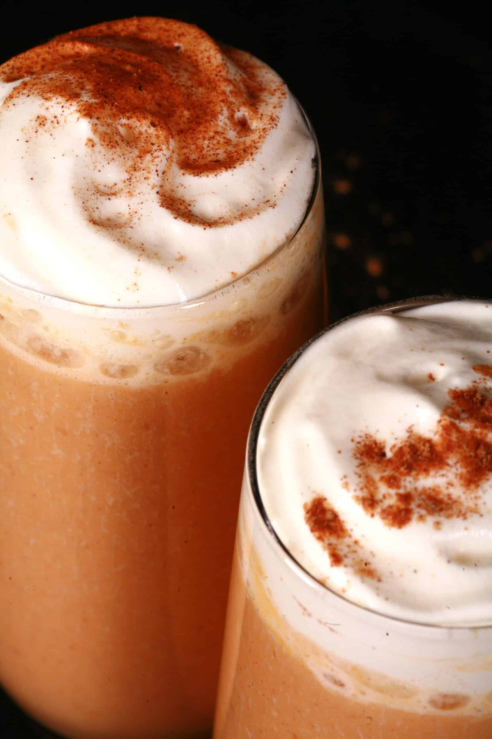 2 pumpkin pie protein smoothies in tall glasses, topped with whipped cream and pumpkin spice.