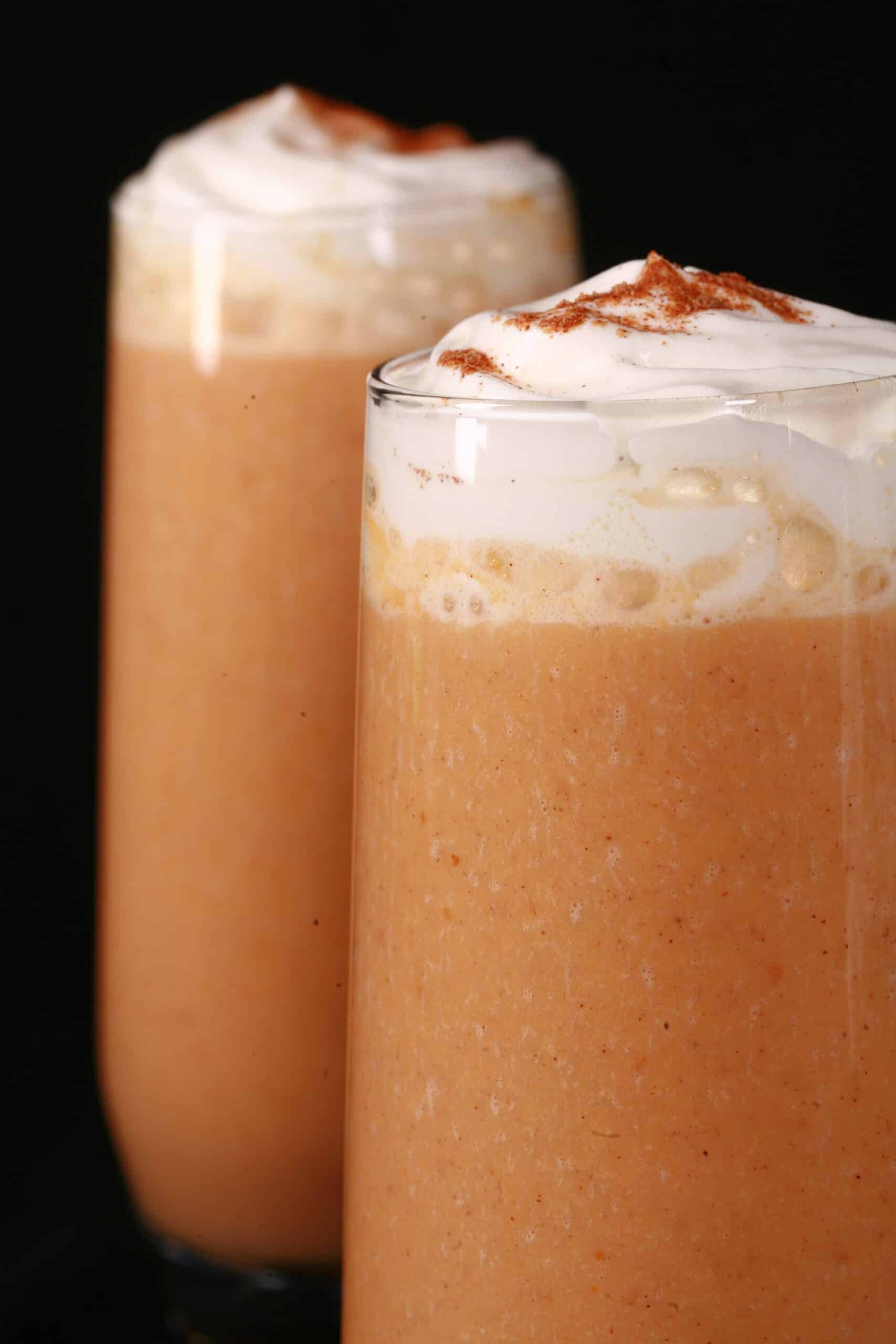 2 pumpkin pie protein shakes in tall glasses, topped with whipped cream and pumpkin spice.