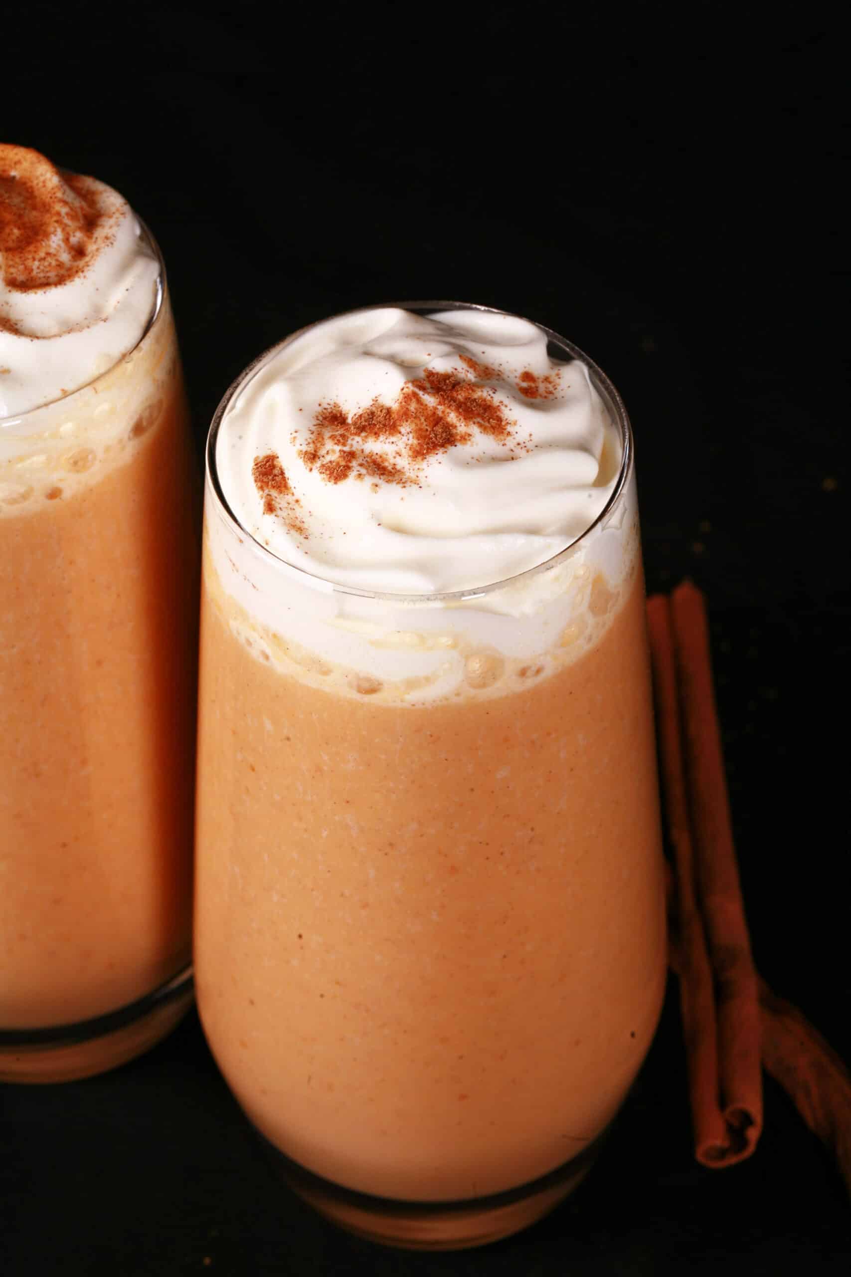2 pumpkin pie protein smoothies in tall glasses, topped with whipped cream and pumpkin spice.