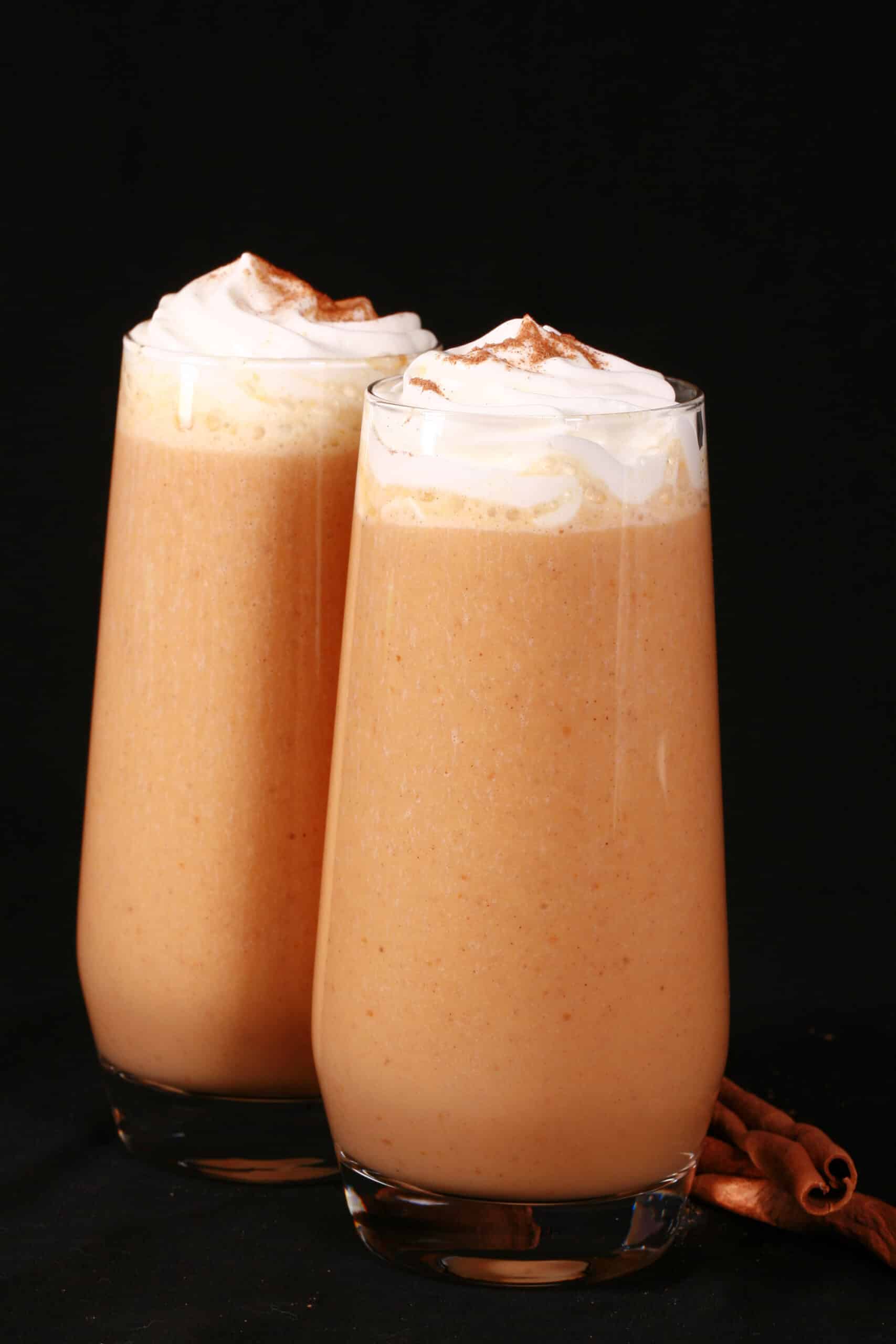 2 pumpkin pie protein shakes in tall glasses, topped with whipped cream and pumpkin spice.