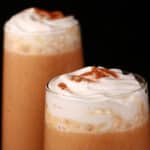 2 pumpkin pie protein smoothies in tall glasses, topped with whipped cream and pumpkin spice.
