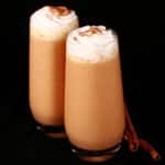 2 pumpkin pie protein shakes in tall glasses, topped with whipped cream and pumpkin spice.