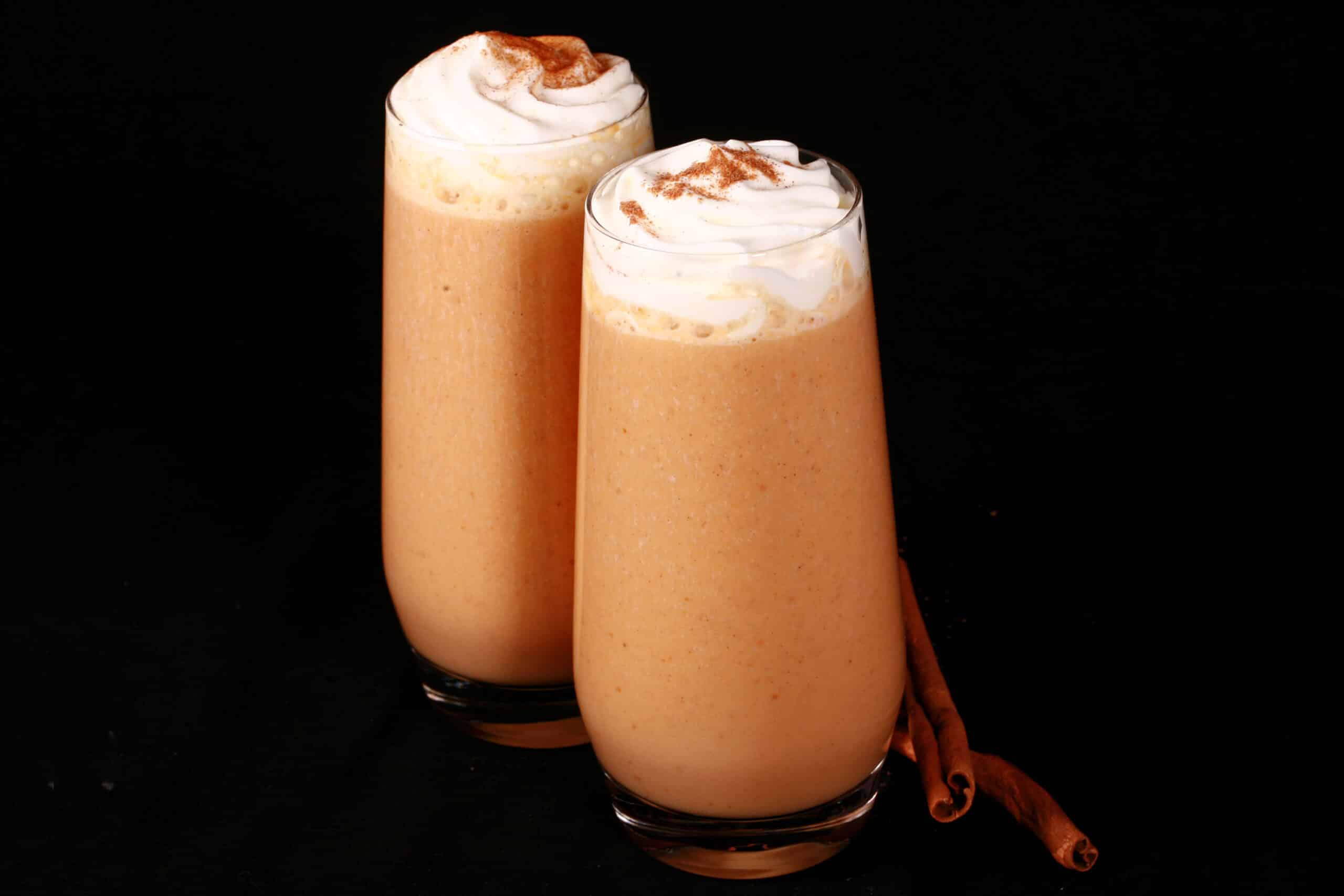 2 pumpkin pie protein shakes in tall glasses, topped with whipped cream and pumpkin spice.