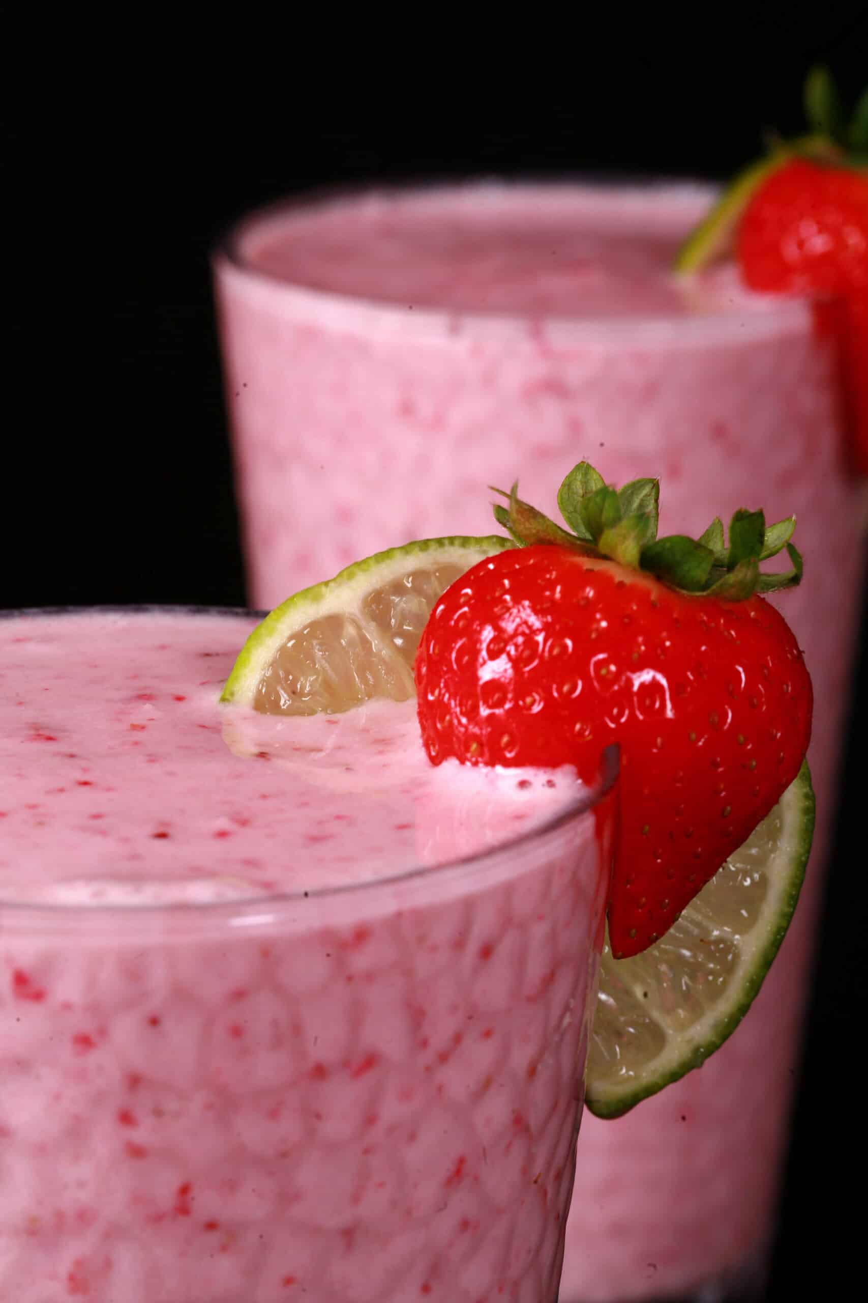 2 tall glasses of non-alcoholic strawberry daiquiri protein smoothies, garnished with a fresh strawberry and a slice of lime.