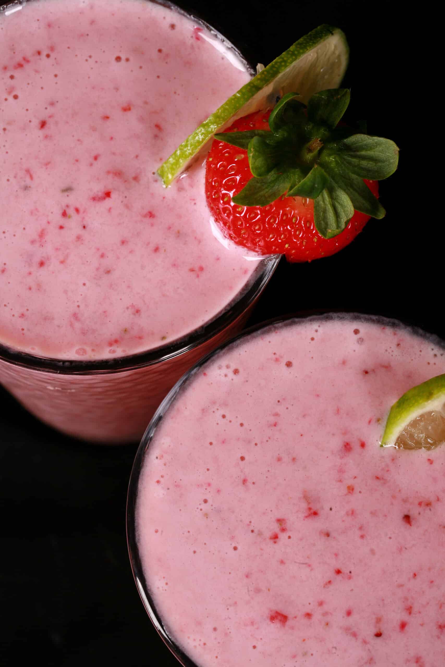 2 tall glasses of non-alcoholic high protein strawberry daiquiri smoothies, garnished with a fresh strawberry and a slice of lime.