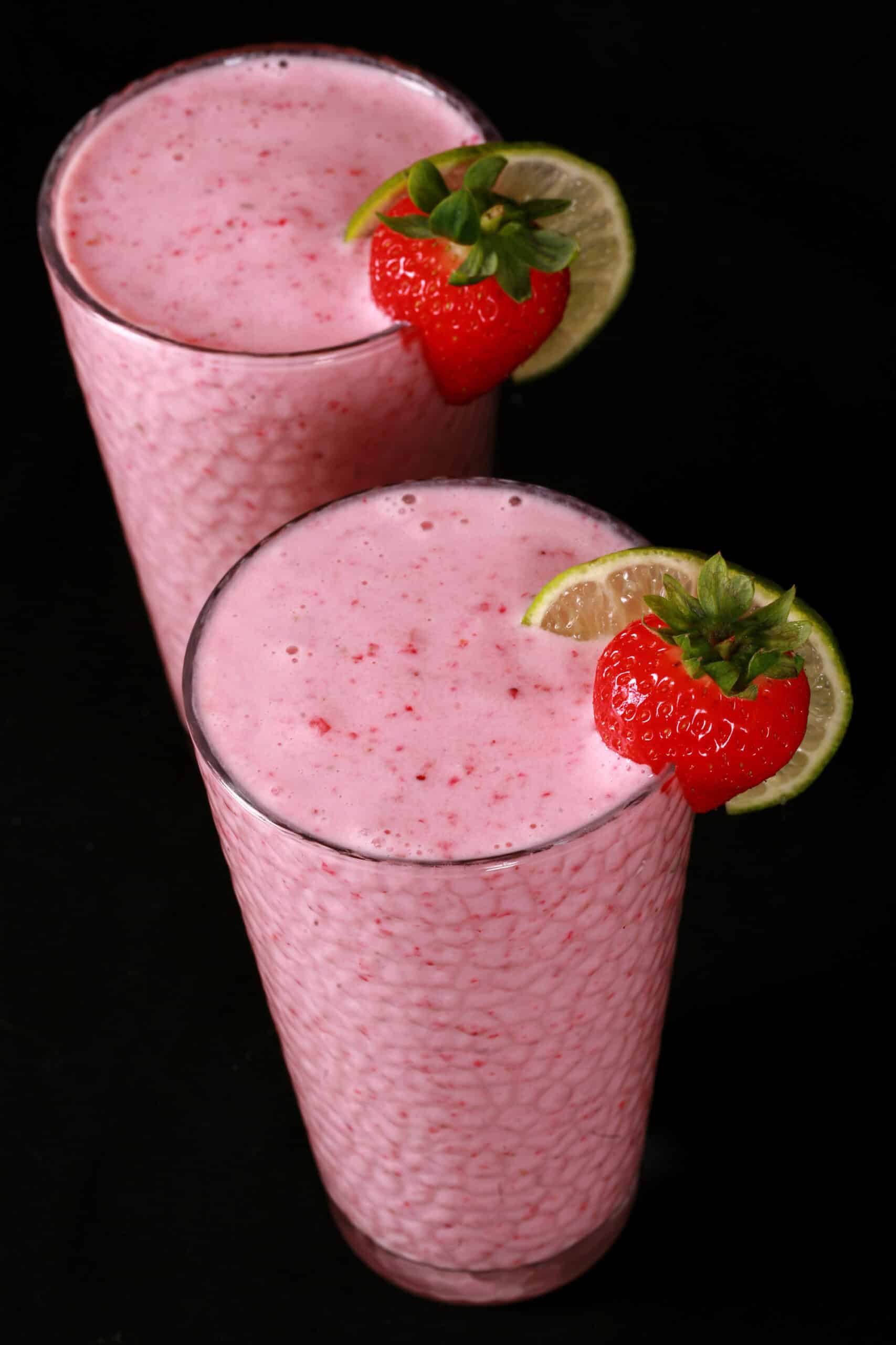 2 tall glasses of non-alcoholic strawberry daiquiri protein smoothies, garnished with a fresh strawberry and a slice of lime.