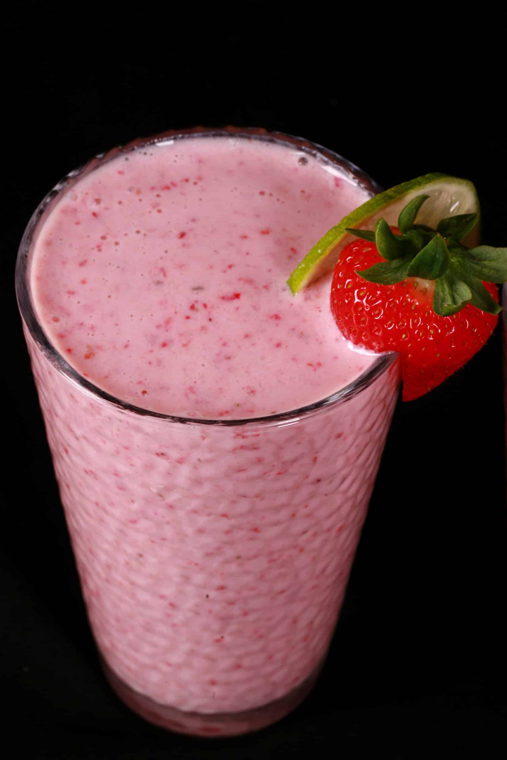 2 tall glasses of non-alcoholic high protein strawberry daiquiri smoothies, garnished with a fresh strawberry and a slice of lime.