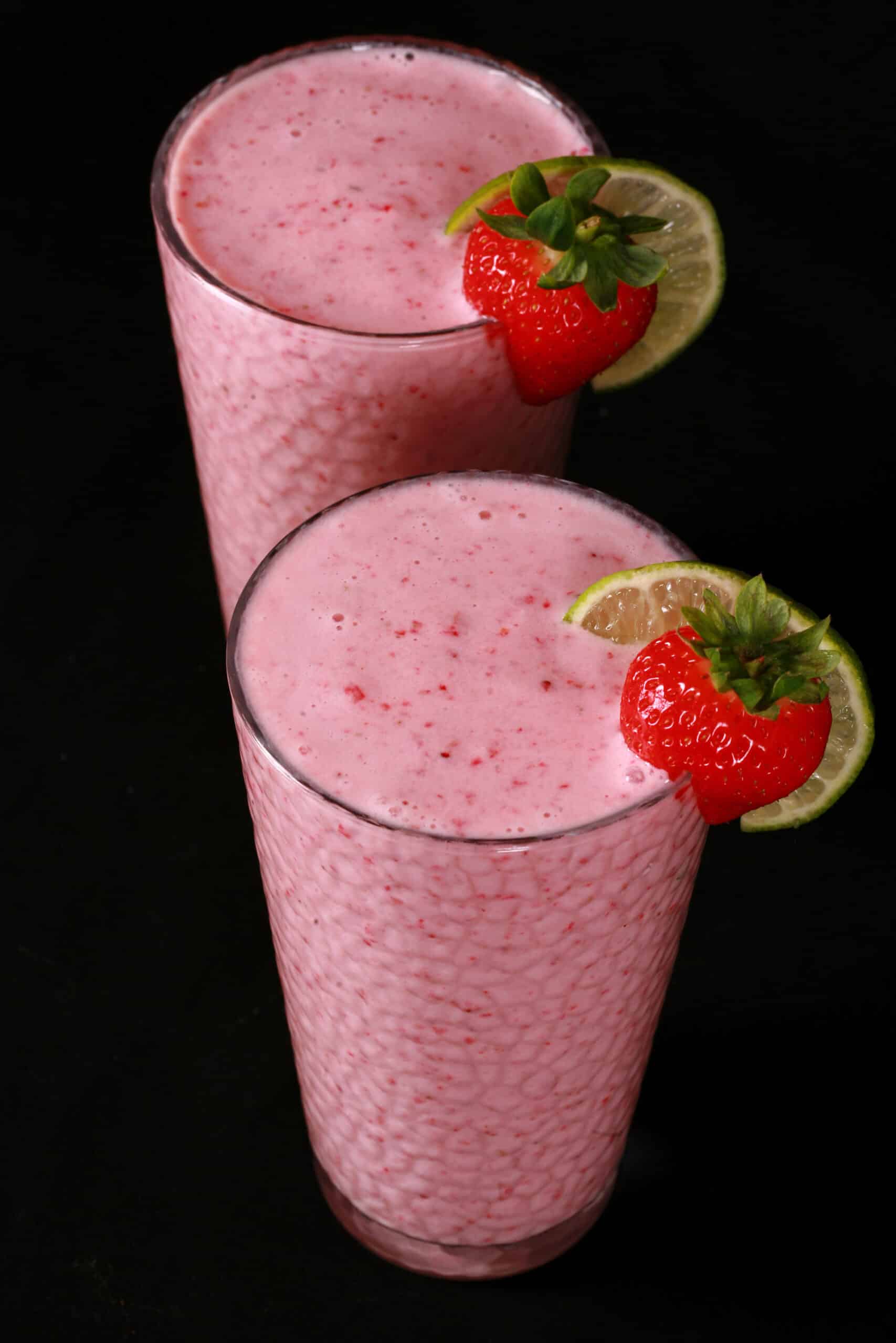 2 tall glasses of non-alcoholic strawberry daiquiri protein smoothies, garnished with a fresh strawberry and a slice of lime.