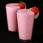 2 tall glasses of non-alcoholic high protein strawberry daiquiri smoothies, garnished with a fresh strawberry and a slice of lime.