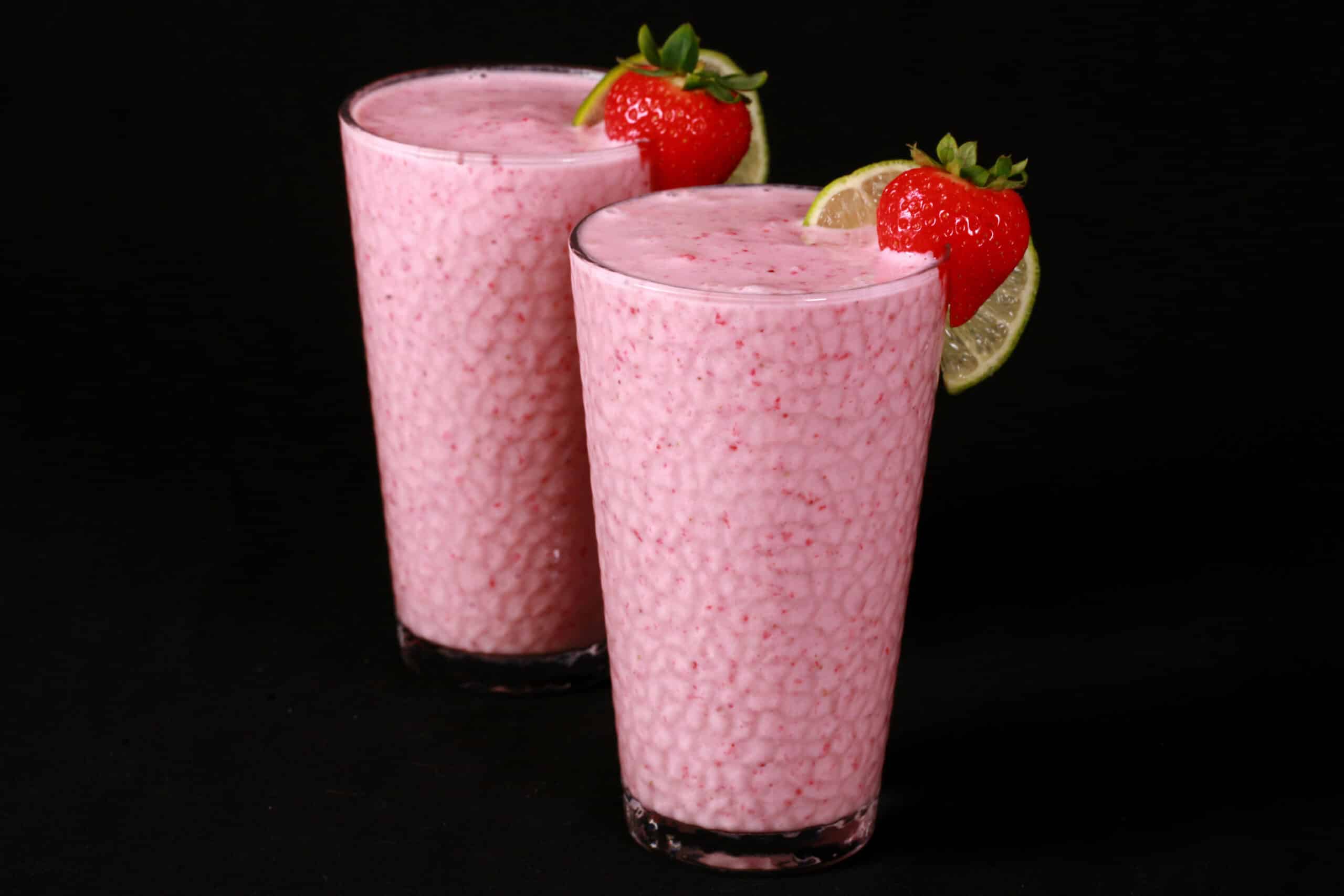 2 tall glasses of non-alcoholic high protein strawberry daiquiri smoothies, garnished with a fresh strawberry and a slice of lime.