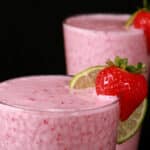 2 tall glasses of non-alcoholic strawberry daiquiri protein smoothies, garnished with a fresh strawberry and a slice of lime.