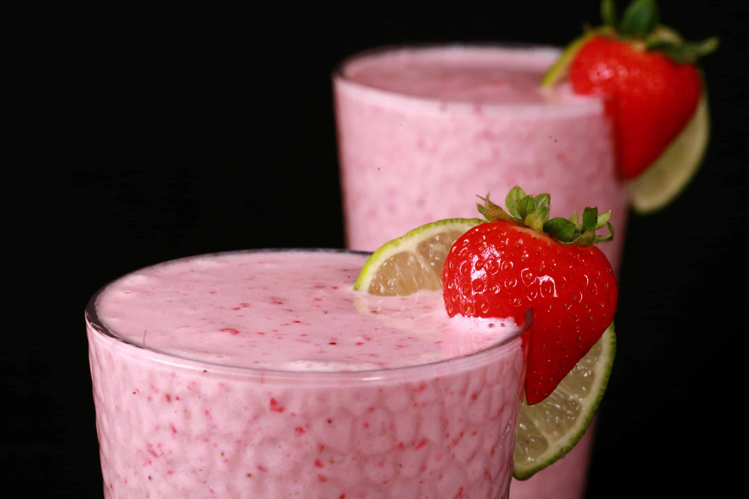 2 tall glasses of non-alcoholic strawberry daiquiri protein smoothies, garnished with a fresh strawberry and a slice of lime.